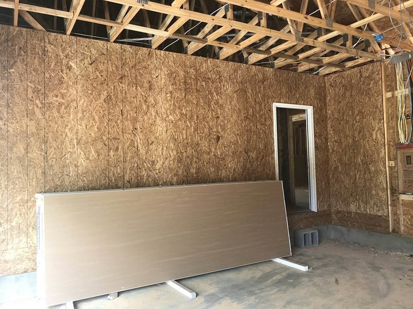 Living space featuring a wood accent wall, white paneling, exposed wooden ceiling beams, plaster walls, and a doorway with composite trim.
