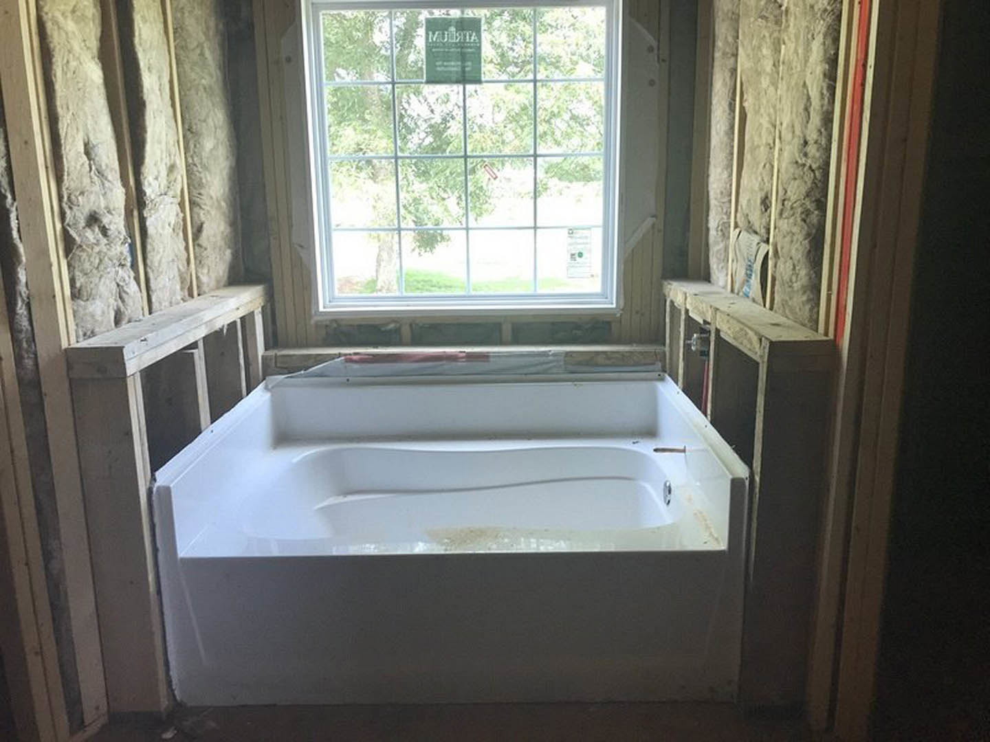 Freestanding white bathtub with visible mold on surface, surrounded by wood-paneled walls, window with sign, chrome faucet, and plumbing fixtures
