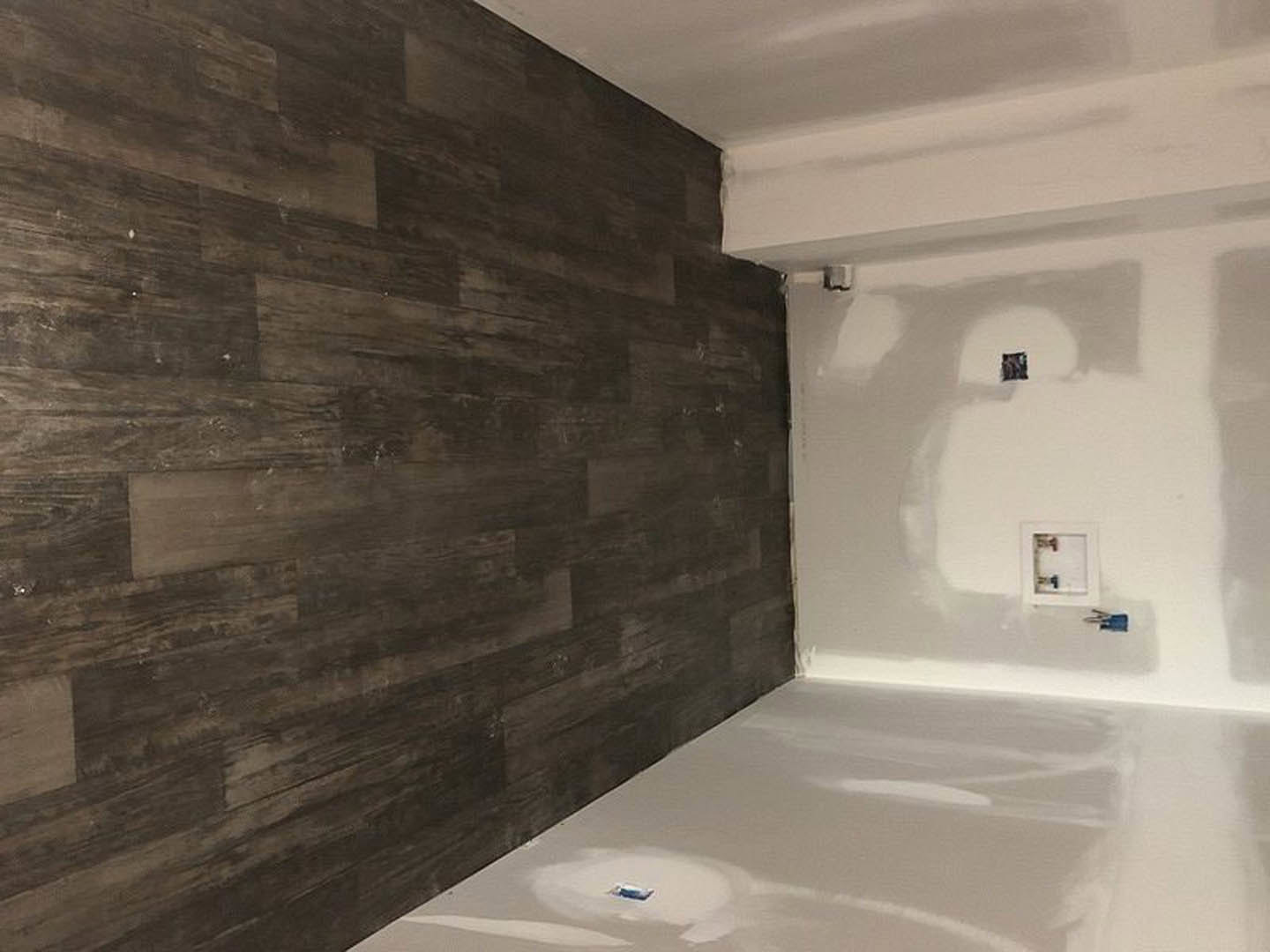 Bathroom with wood accent wall, white painted walls, white tile floor, freestanding blue bathtub, recessed ceiling light, and modern plumbing fixtures