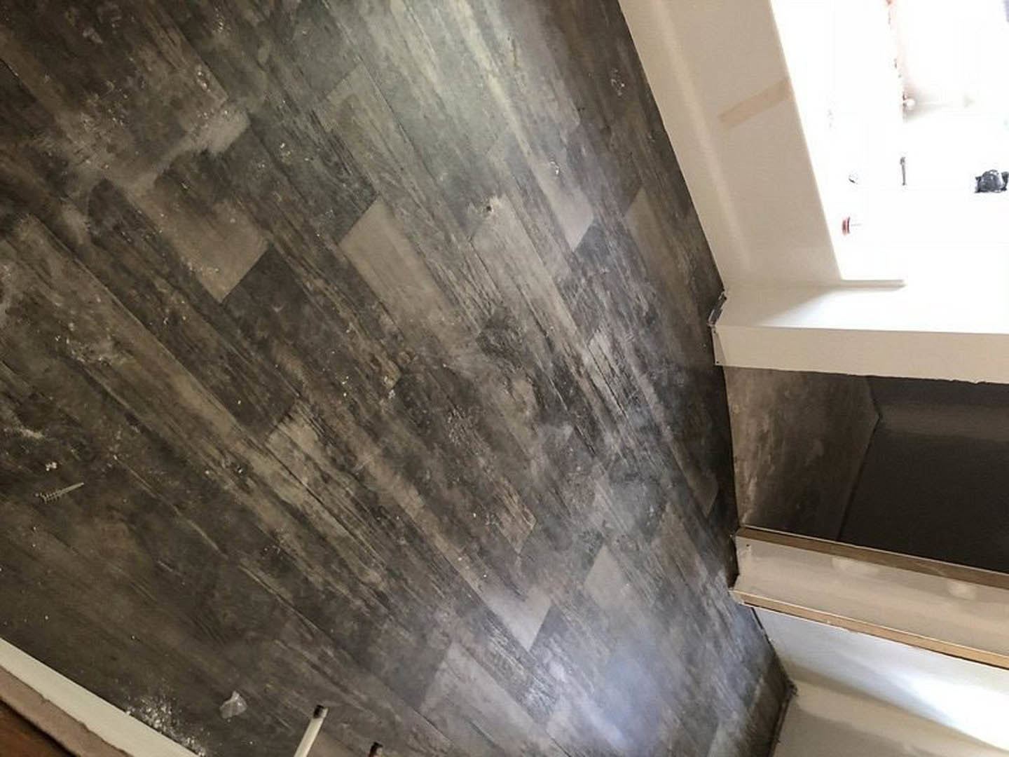 Wood plank flooring, white door, white plaster walls, window letting in natural light, plastic bag on white surface, black background.