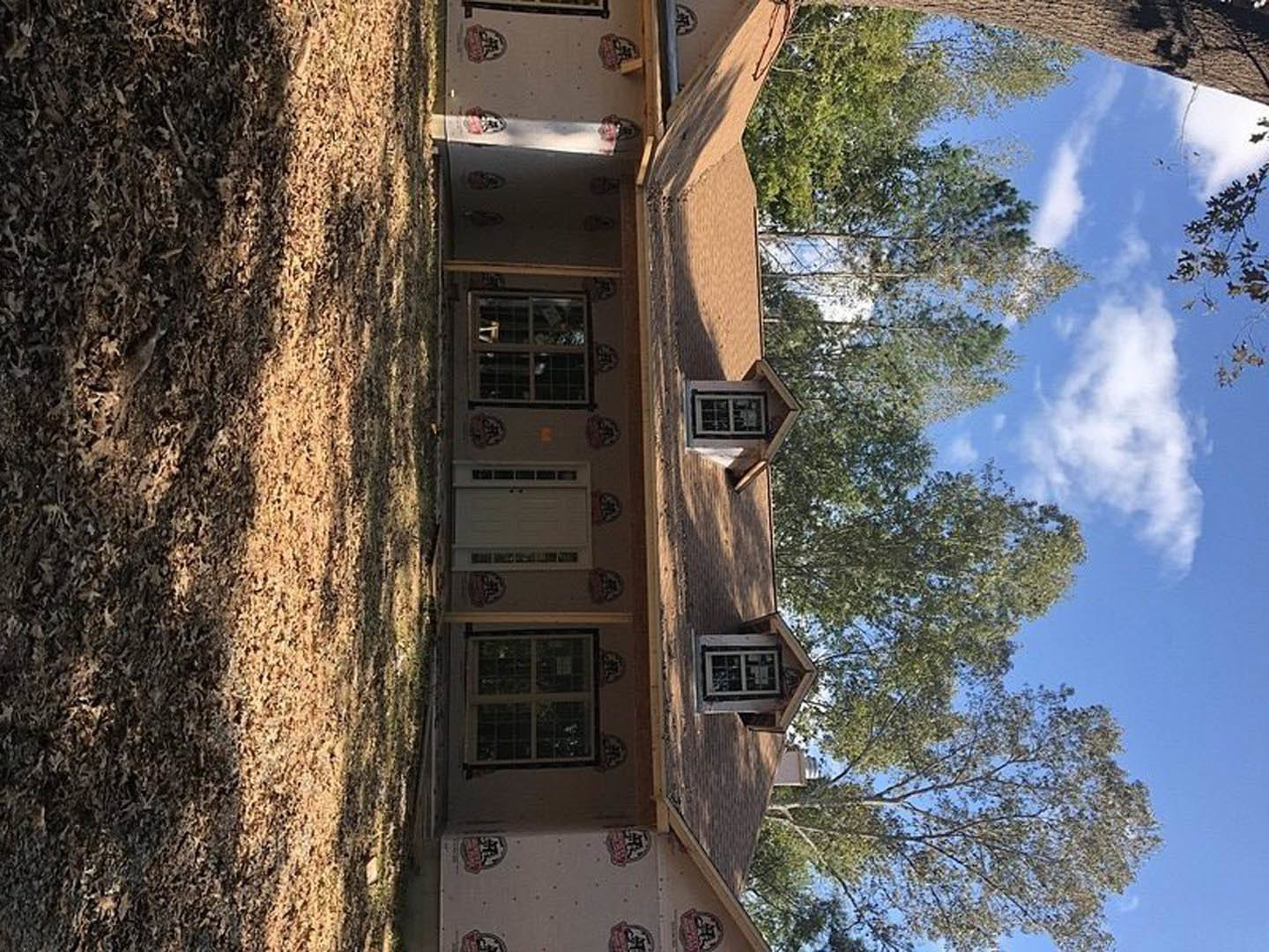 Modern home exterior with large windows, light-colored siding, and a leafy tree in the background under a partly cloudy sky