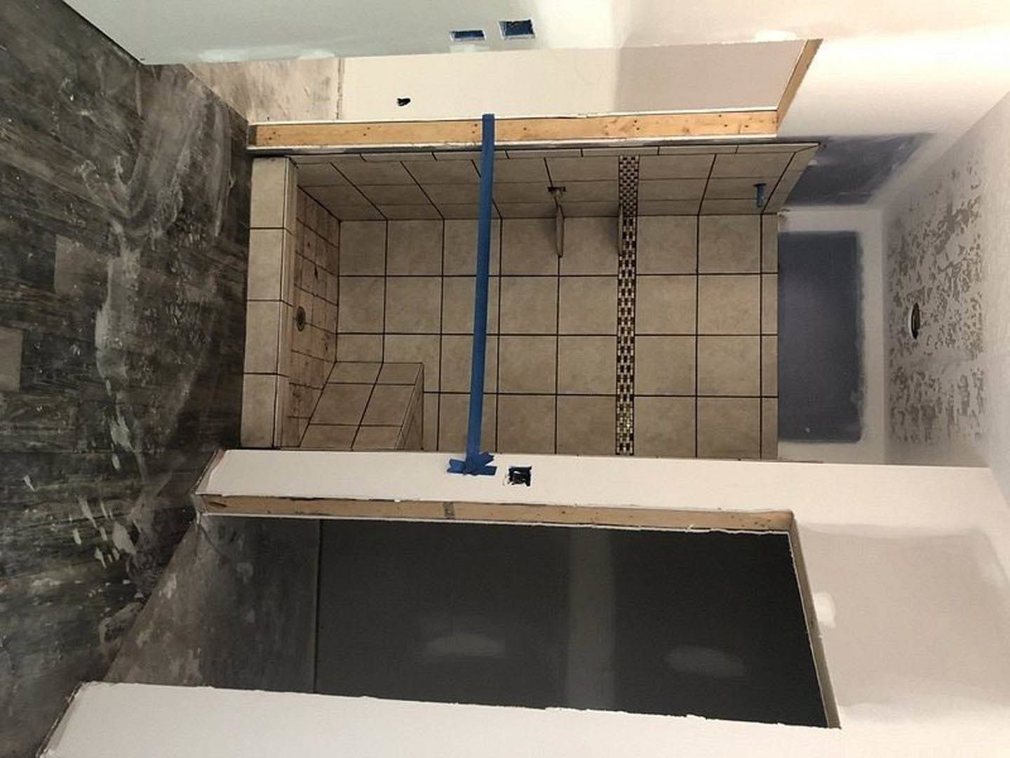 Bathroom with light tile floor, blue accent stripe on wall tile, marble countertop, wooden-framed mirror, and modern plumbing fixtures.