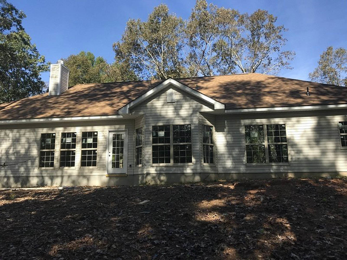 Two-story house with white siding, multi-pane windows, and a white front door, surrounded by leafy trees and scattered leaves on the ground