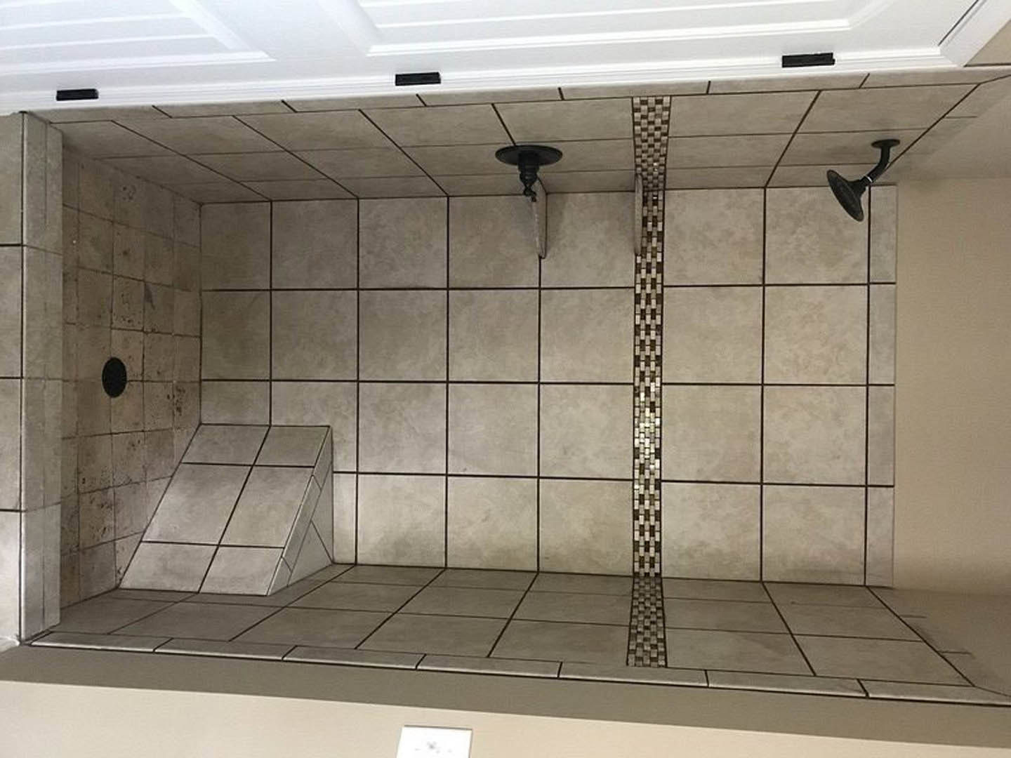 Modern bathroom with grey tiled walls, walk-in shower featuring chrome shower head, white sink with sleek black oval faucet, and plaster ceiling