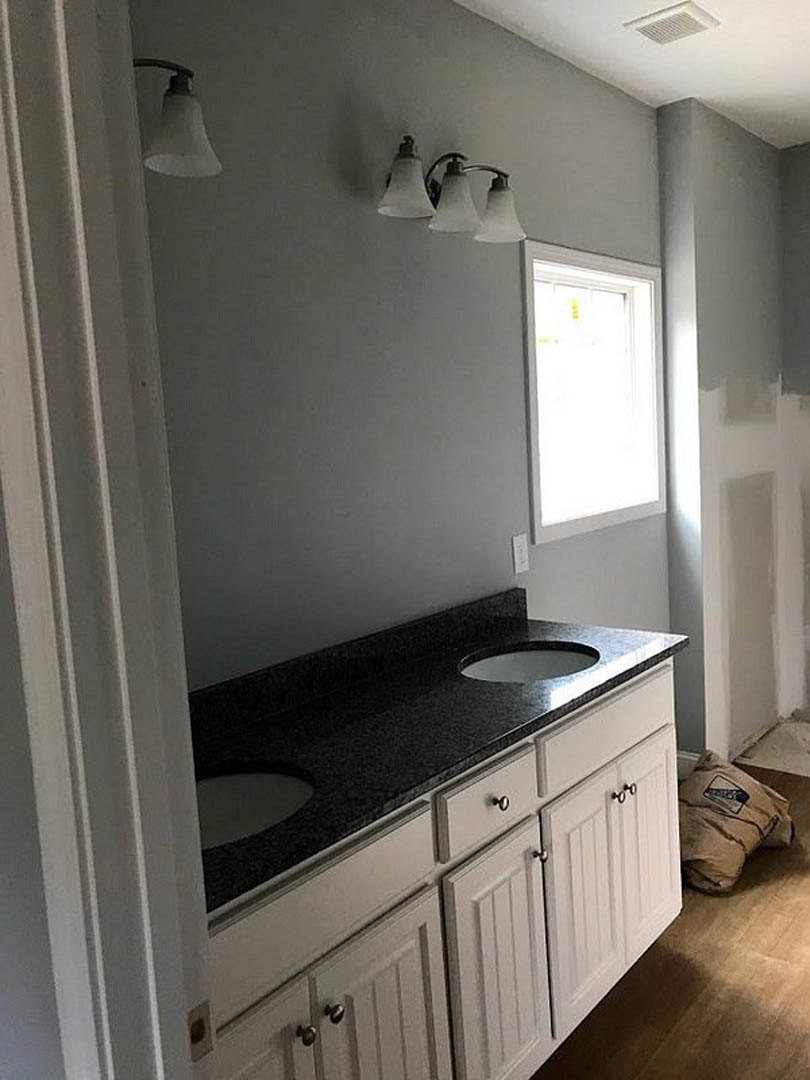 Double vanity bathroom with white sinks, dark stone countertop, wood cabinetry, wall-mounted lights, and tile flooring.