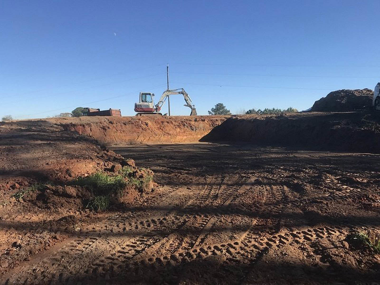 Bulldozer and crane on dirt construction site, tire tracks visible in soil, machinery with metal bucket, open sky overhead