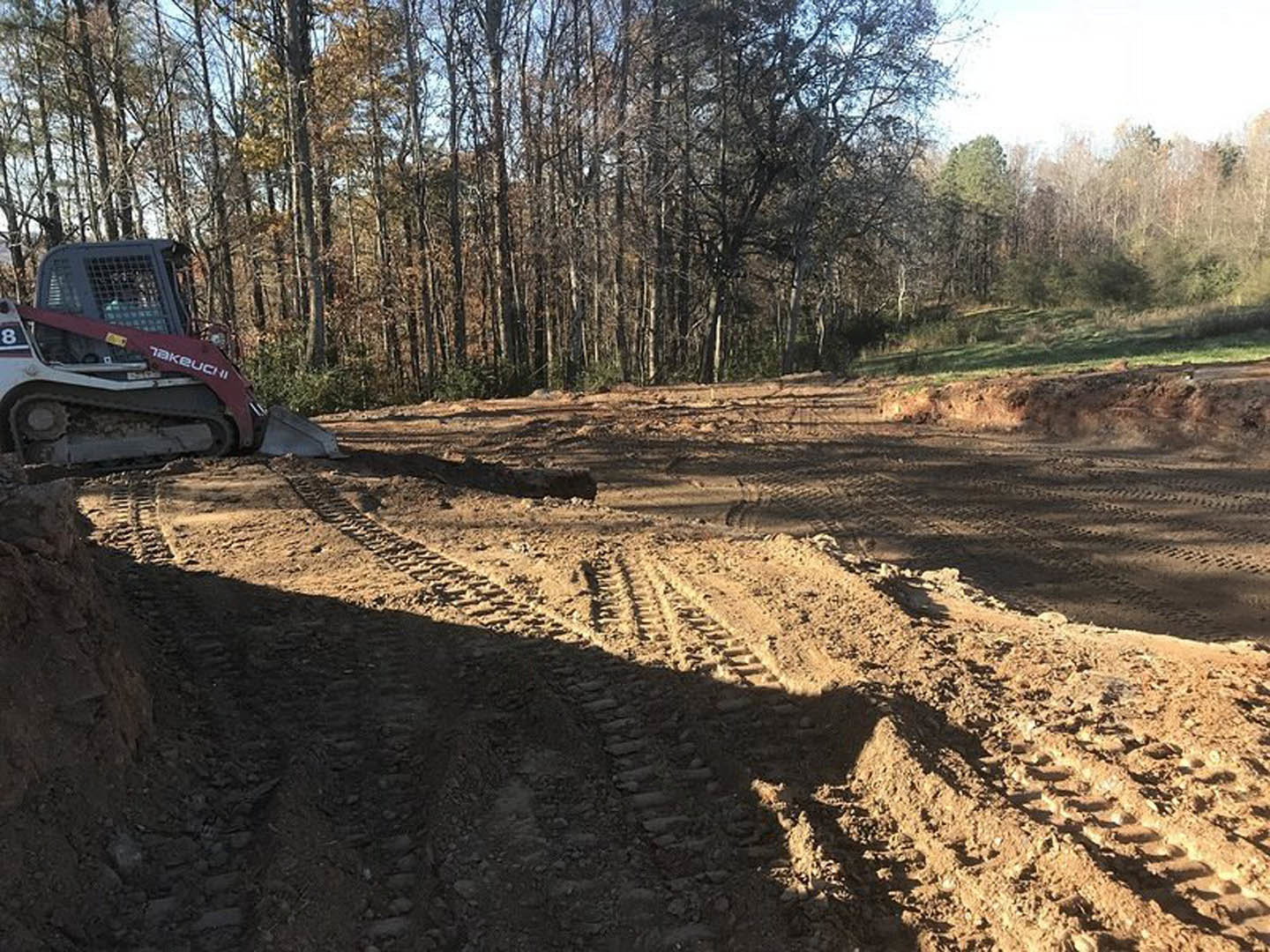 Yellow tractor with large tires parked on a dirt road, surrounded by tire tracks and dense forest trees under a clear sky