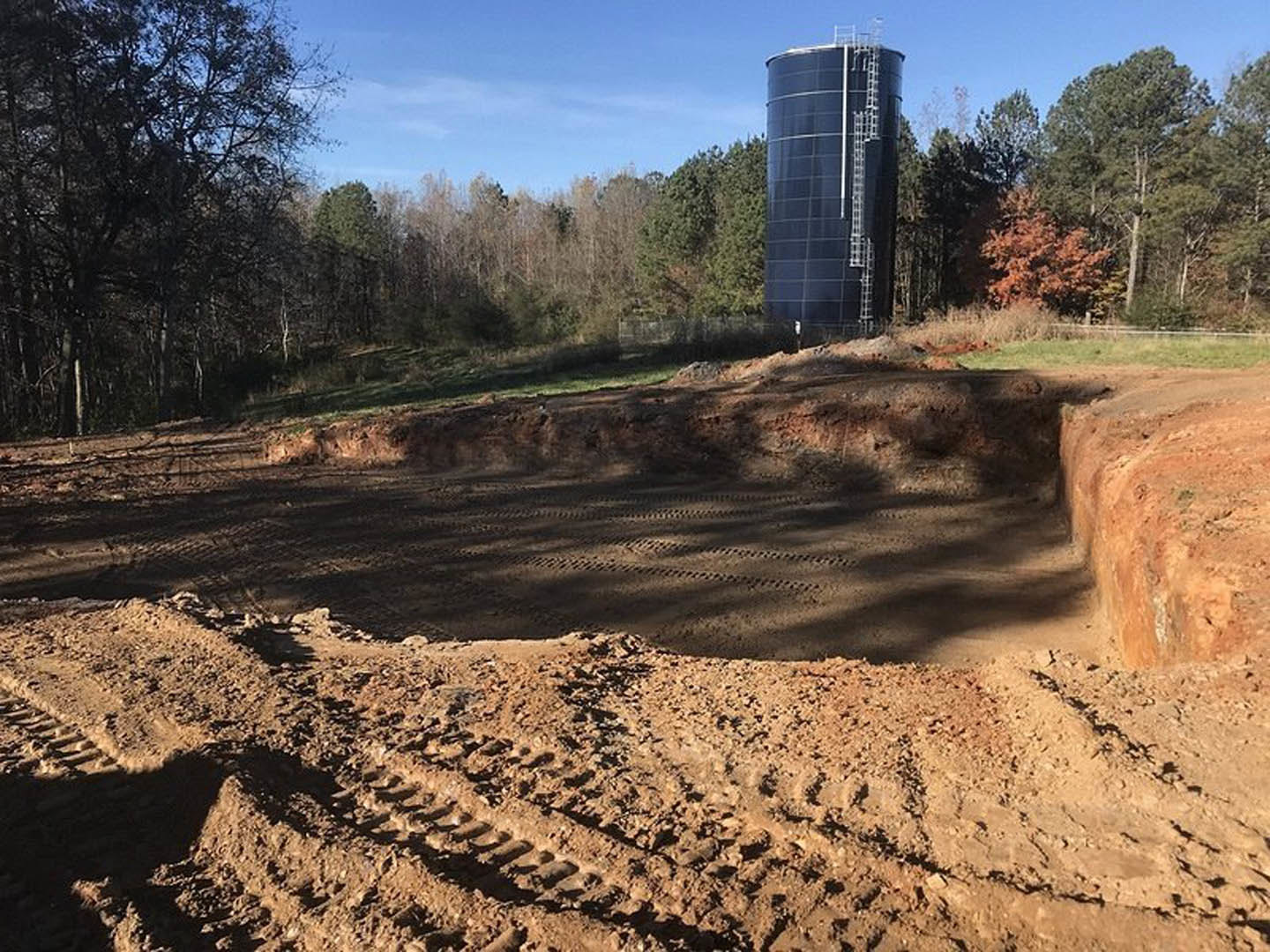 Tall building with ladder, dirt pit and tire tracks in foreground, blue sky with scattered clouds, trees lining the background