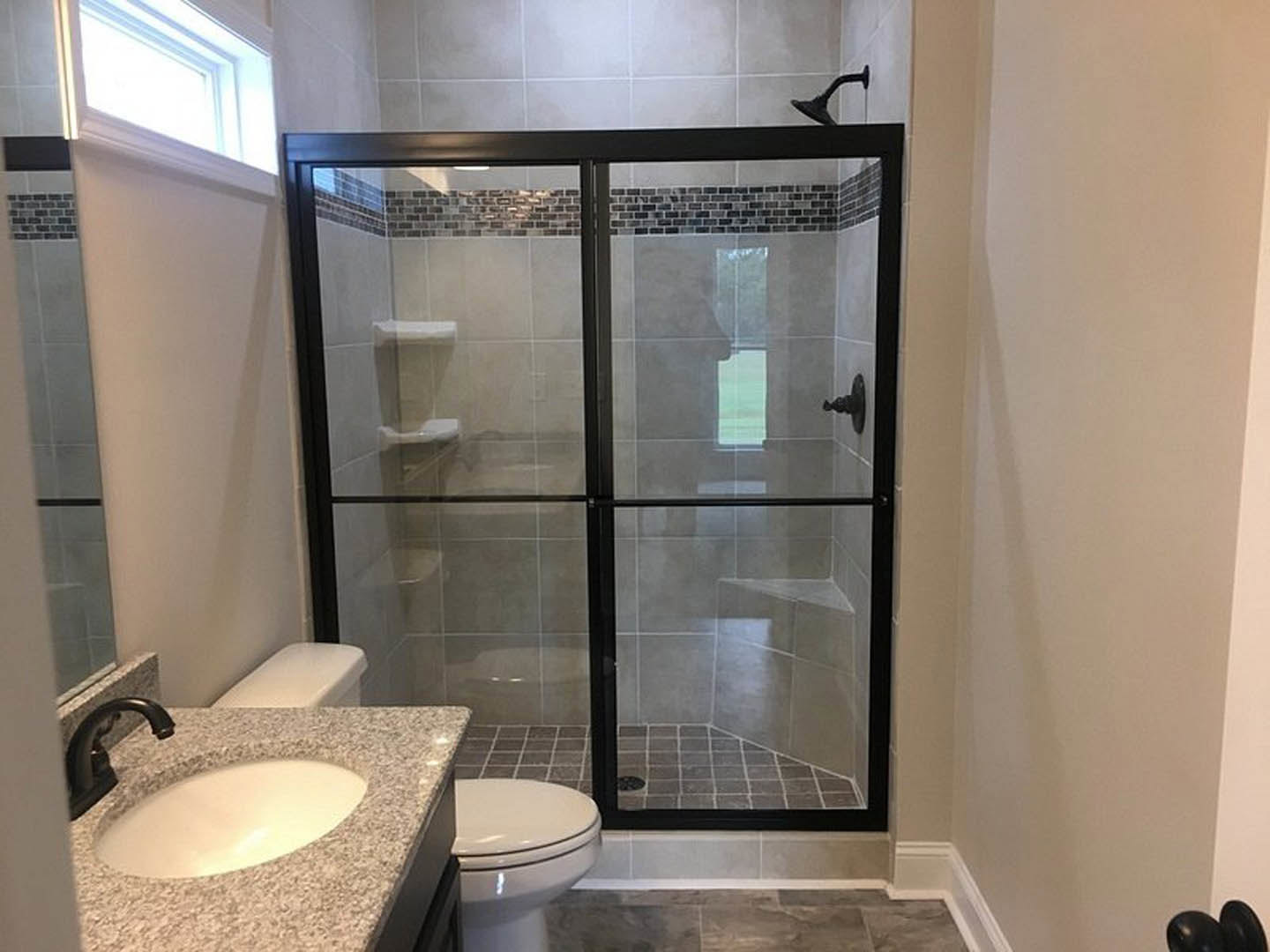 Modern bathroom featuring a frameless glass shower door, white ceramic sink with chrome faucet, tiled walls, and a close-up view of a toilet and brushed metal door knob