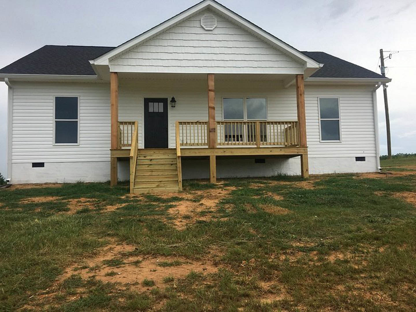 White siding house with covered porch, black front door, white framed windows, grassy front yard, and blue sky background