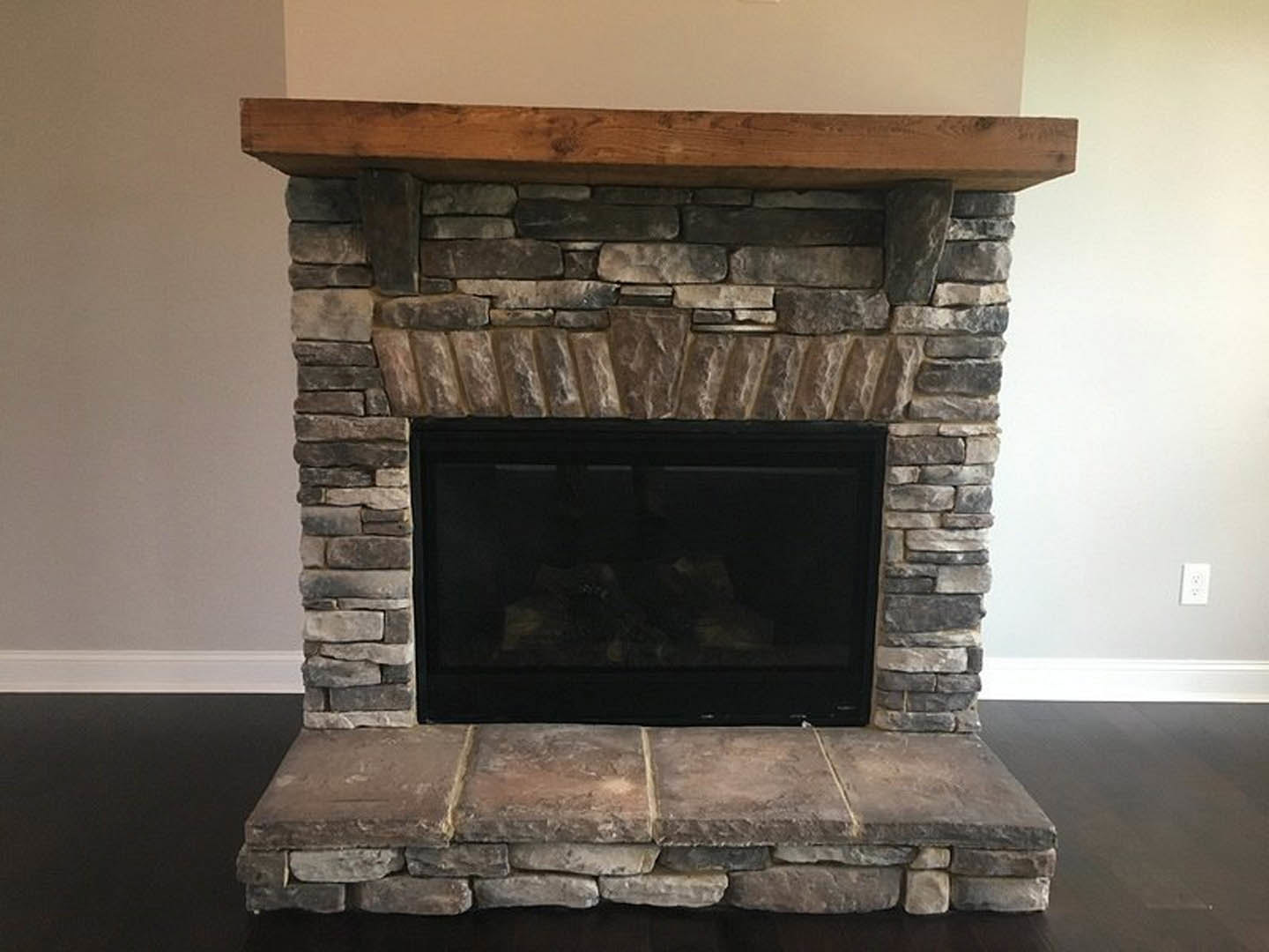 Stone fireplace with glass door and wood mantel shelf, surrounded by textured stone wall and exposed wood beam in a sitting room