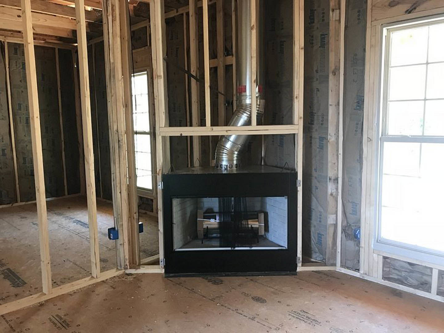 Living room with black metal fireplace, wood flooring, exposed wood ceiling beams, large window, and metal pipe along wall