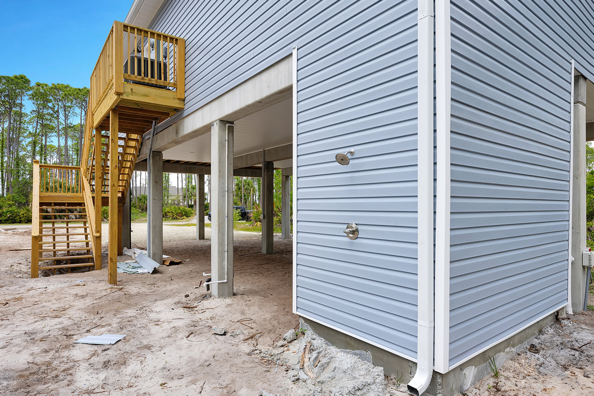 Wooden deck and stairs attached to a grey-sided house under construction, porch with wooden railing, trees and sky in the background