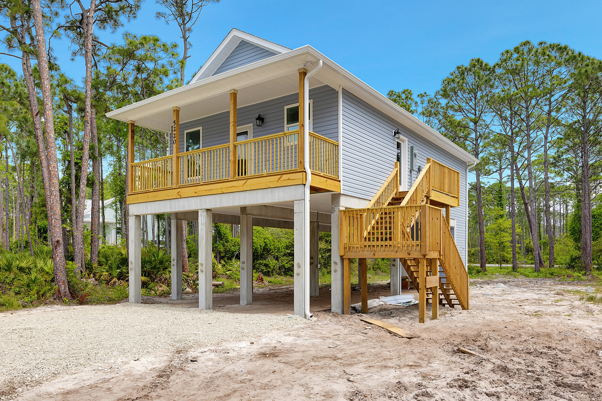Two-story house with wooden porch and stairs, surrounded by trees, rabbit resting on grassy ground in front