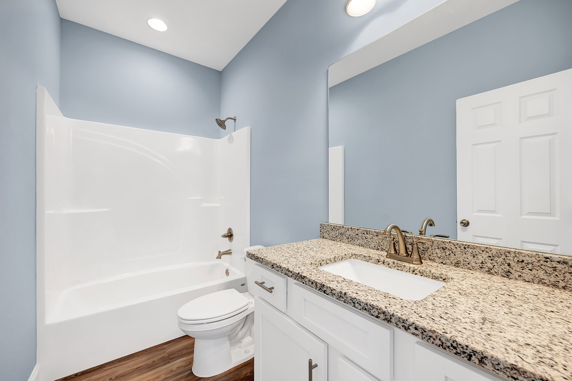 Bathroom with marble countertop, white bathtub, white toilet, wood flooring, square panel door, and sink with chrome tap