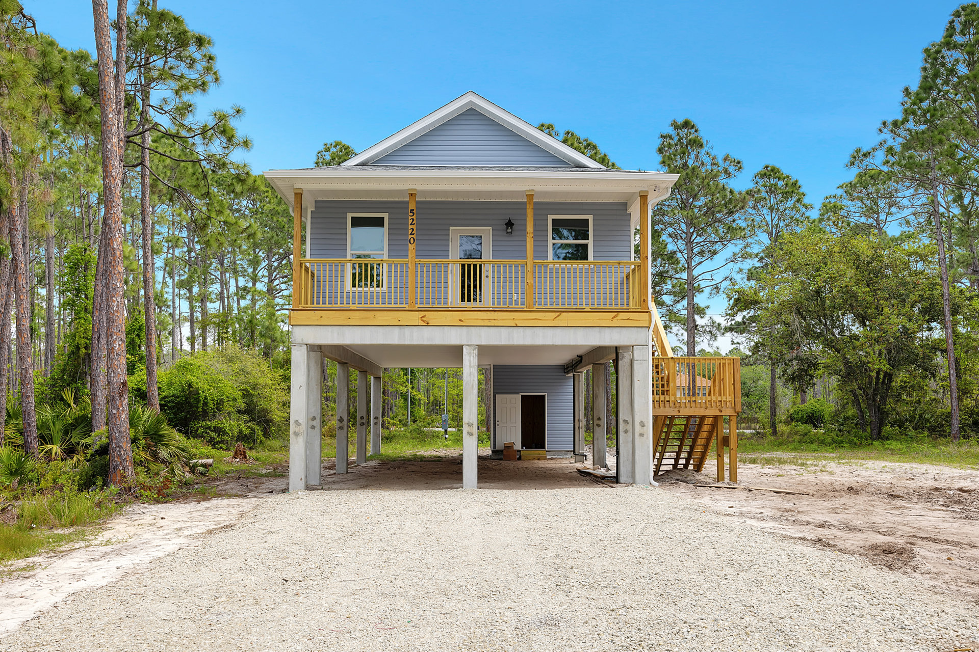 Two-story house with covered front porch, wooden deck, yellow railing, attached garage, and mature tree in landscaped yard