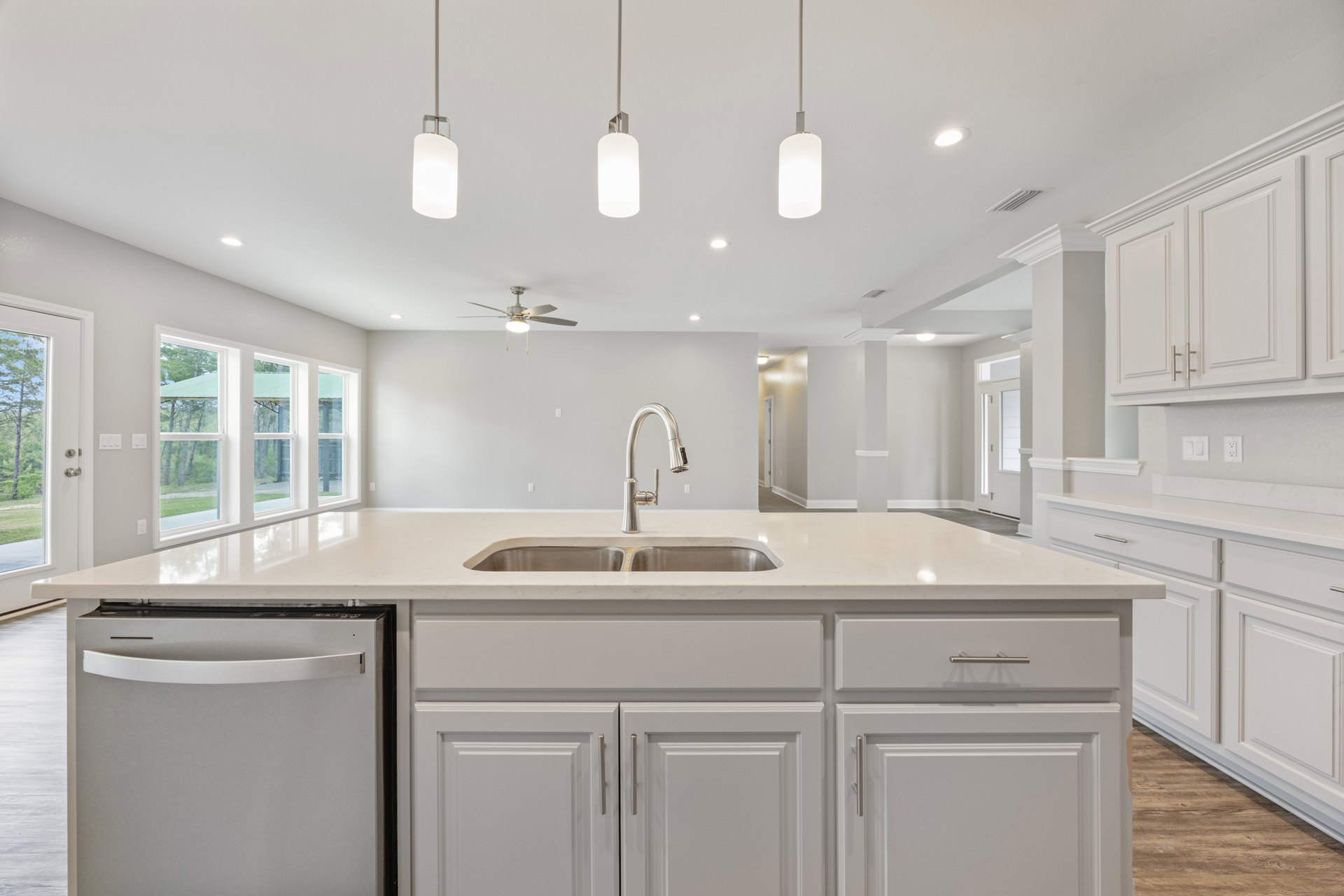 Modern kitchen with white tile backsplash, stainless steel dishwasher with handle, undermount sink, chrome faucet, white cabinetry, and stone countertop