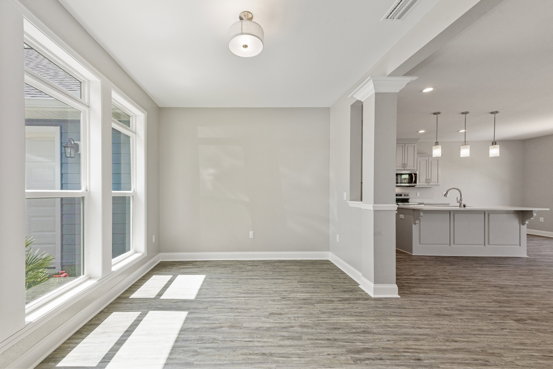Open kitchen with white cabinets, stainless steel microwave, wood flooring, and modern ceiling light fixture.