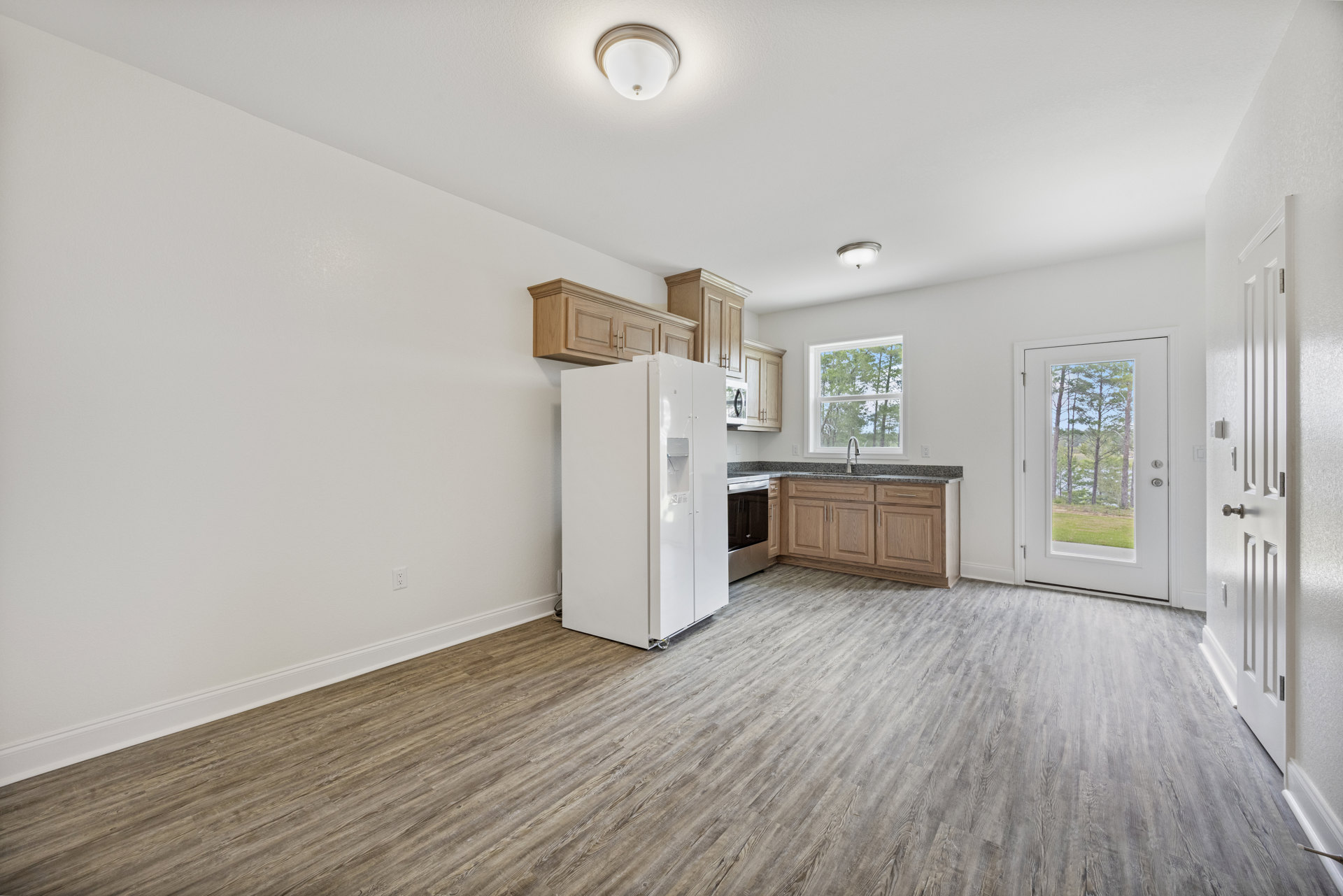Kitchen with wood flooring, white refrigerator, black oven, white cabinetry, and a window and door offering views of trees and grass outside