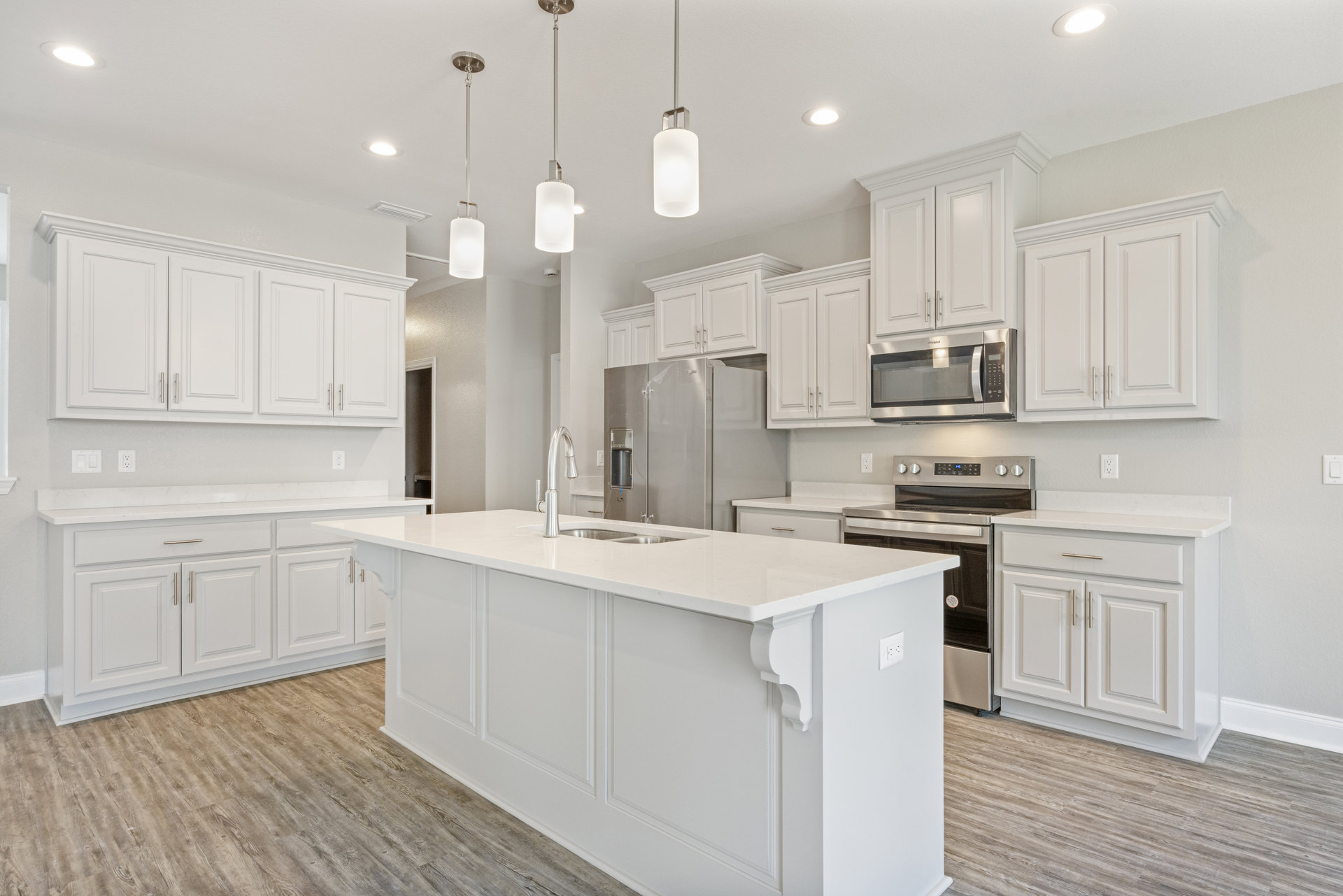 White kitchen with shaker cabinets, stainless steel refrigerator, built-in microwave, large central island with quartz countertop, undermount sink, pendant lighting, and hardwood
