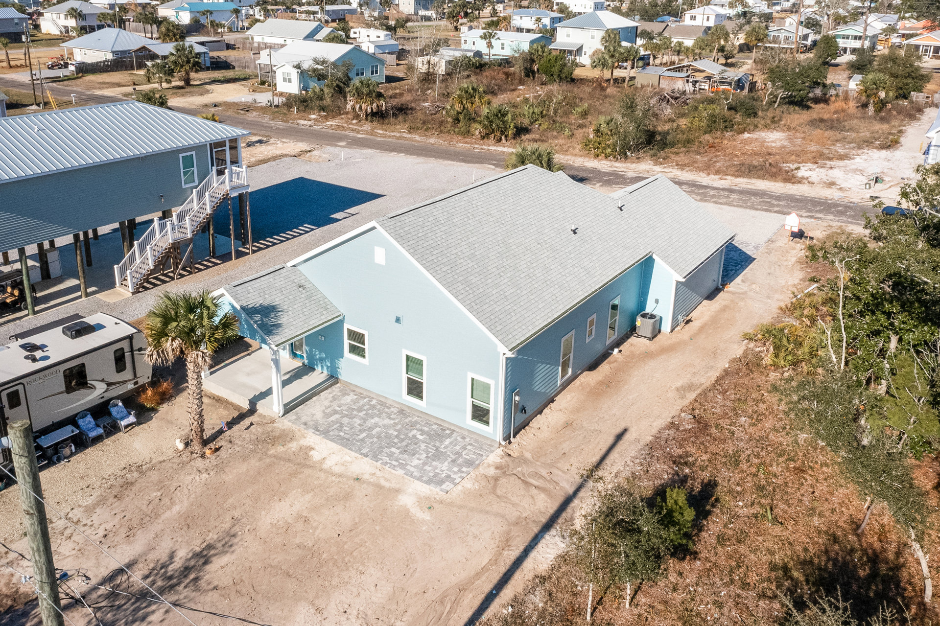 Blue siding house with white roof, driveway, palm tree, and stairs leading to entrance, surrounded by a few trees.