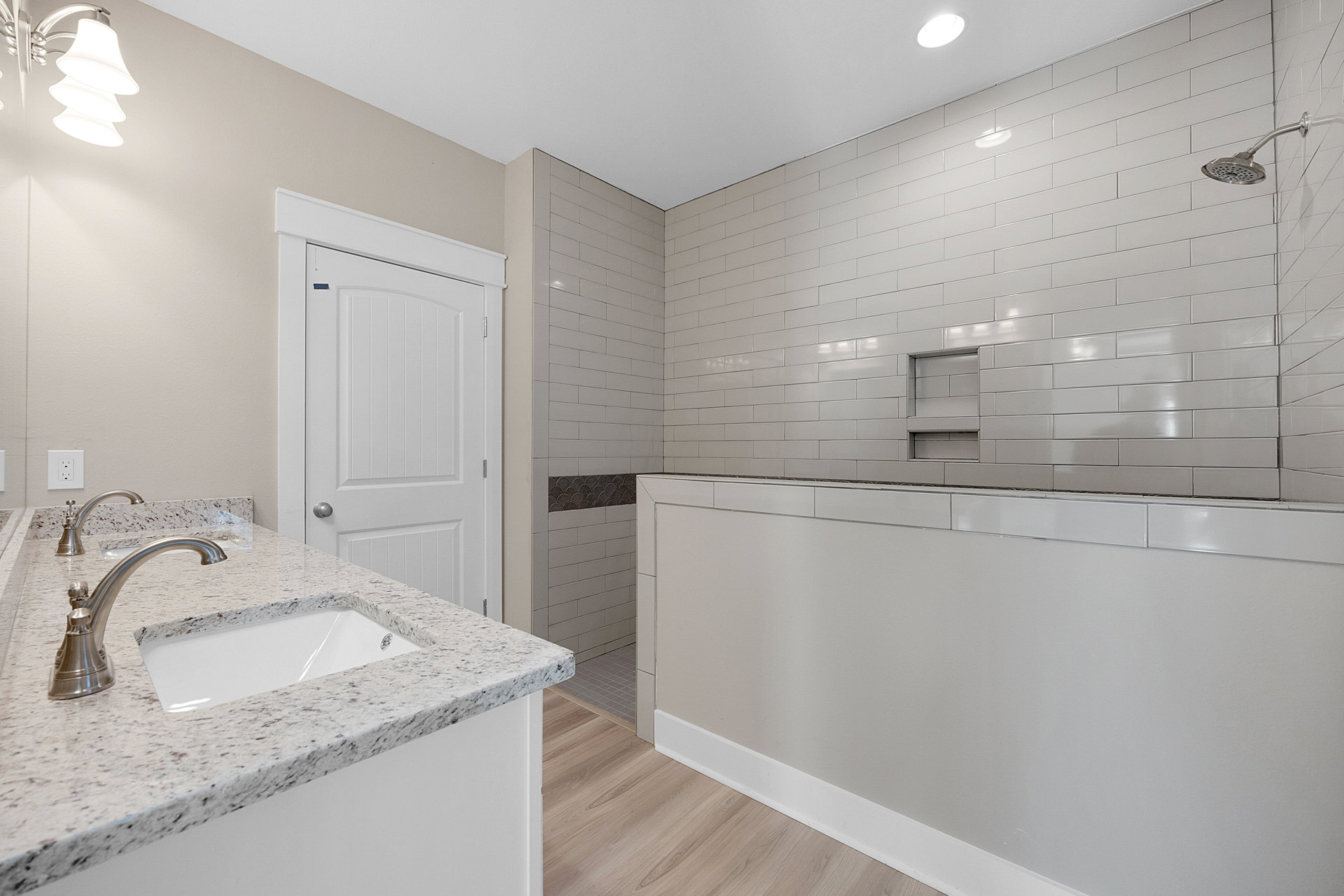 White bathroom vanity with undermount sink, polished chrome faucet, and smooth white countertop; tiled backsplash and wall outlet visible.