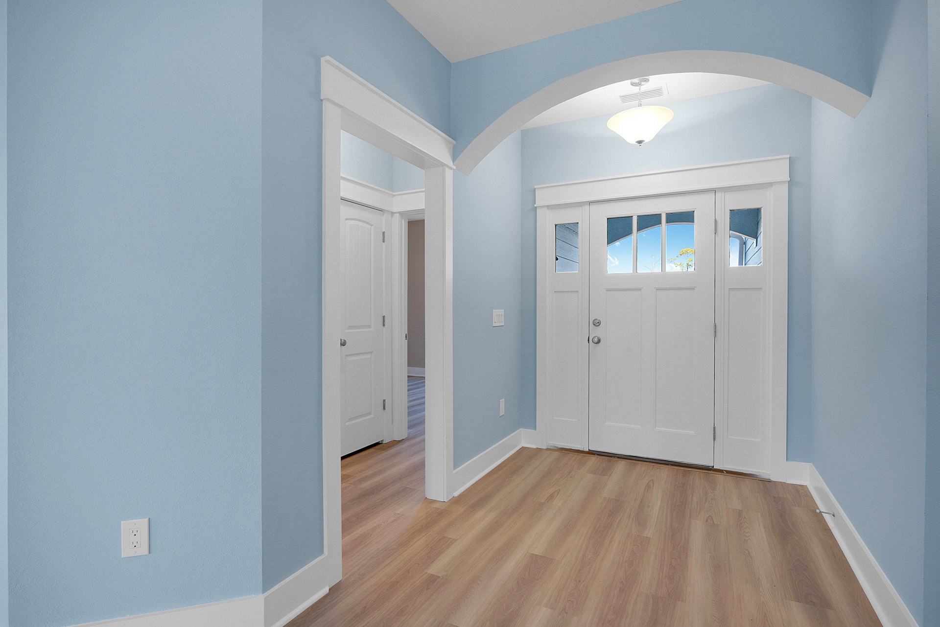 Hallway featuring white paneled doors, wood laminate flooring, white wall molding, and a window showing blue sky and clouds; includes close-ups of a white electrical outlet and a
