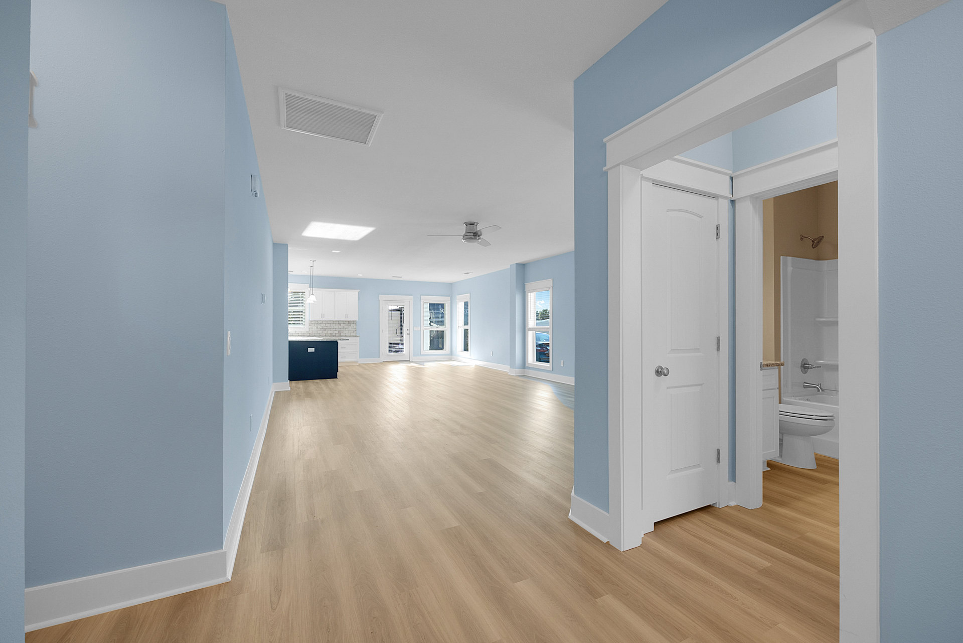 Spacious room with wood flooring, white walls, white door, ceiling fan, blue countertop, light switches, and vent