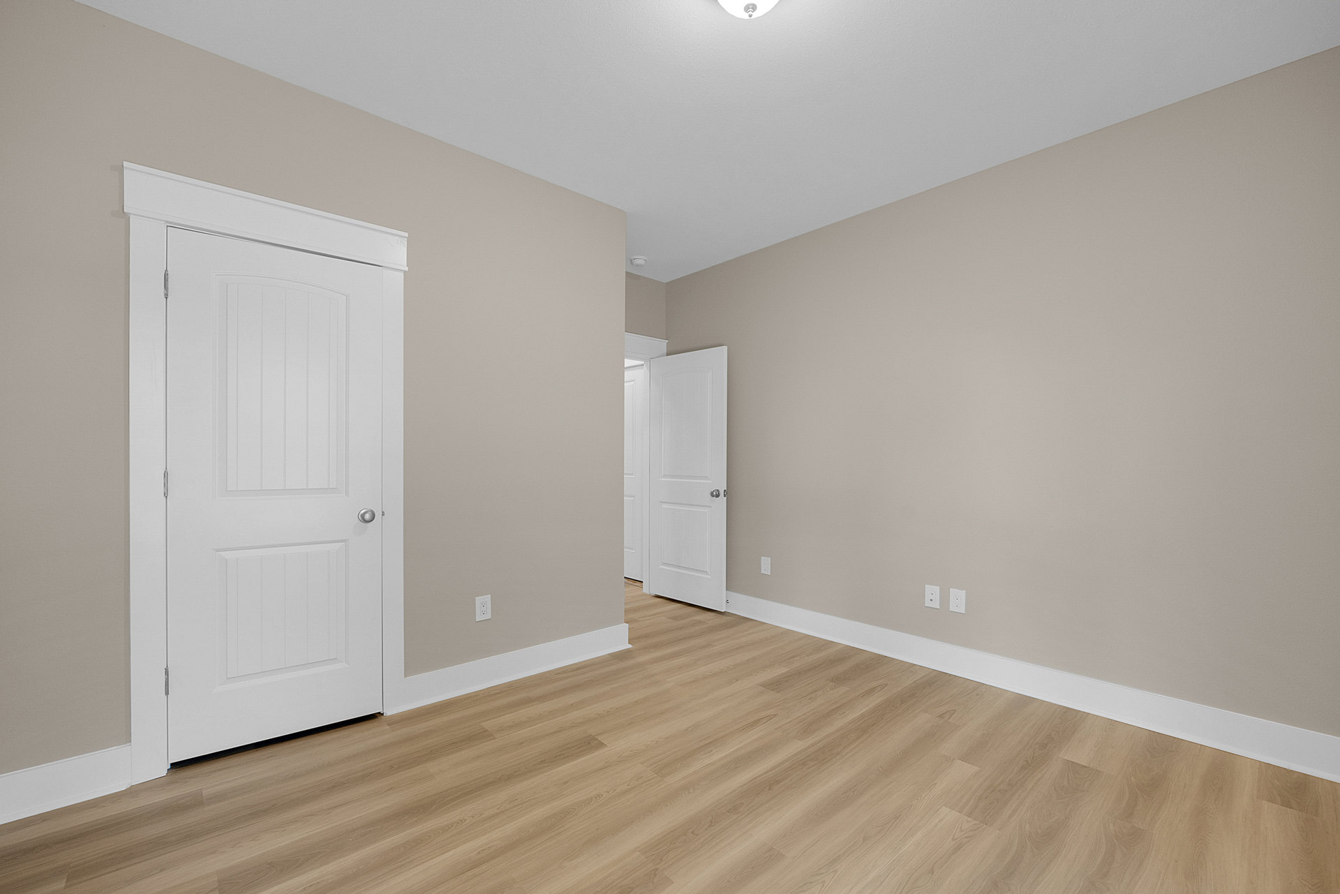 White paneled doors with silver handles, light brown wood flooring, white baseboard trim, and smooth plaster walls