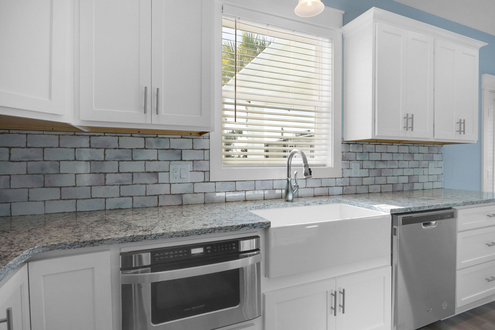 White cabinetry kitchen with stainless steel refrigerator, built-in microwave, sink with chrome faucet, light fixture, and window with blinds above the countertop.