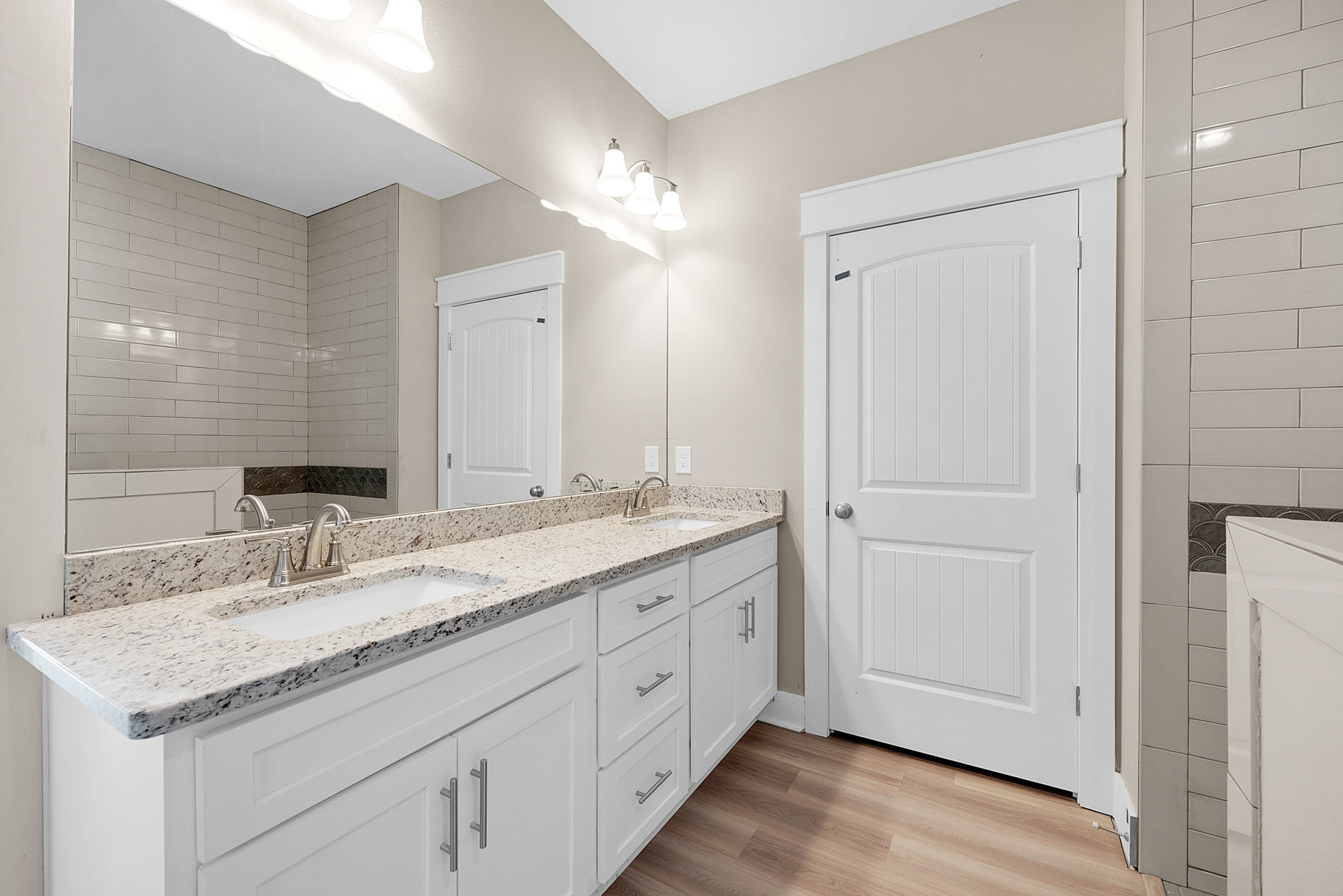 Bathroom with double vanity featuring white sinks, stone countertop, large wall mirror, tile flooring, and white door with silver knob