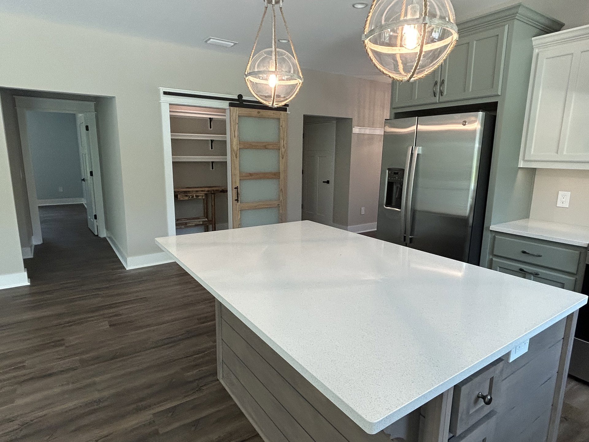 White kitchen island with quartz countertop, stainless steel refrigerator, glass globe pendant light, wood panel door, white cabinetry, and light hardwood flooring