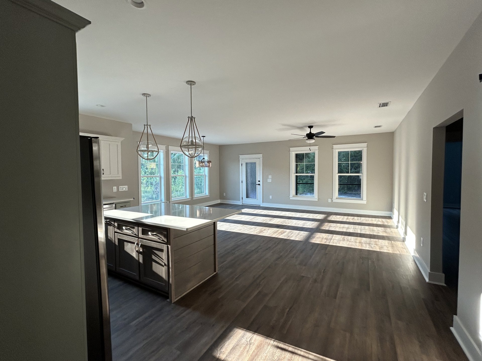 Spacious kitchen with wood flooring, central island with white cabinetry, large window with white frame, glass-paneled door, and modern appliances