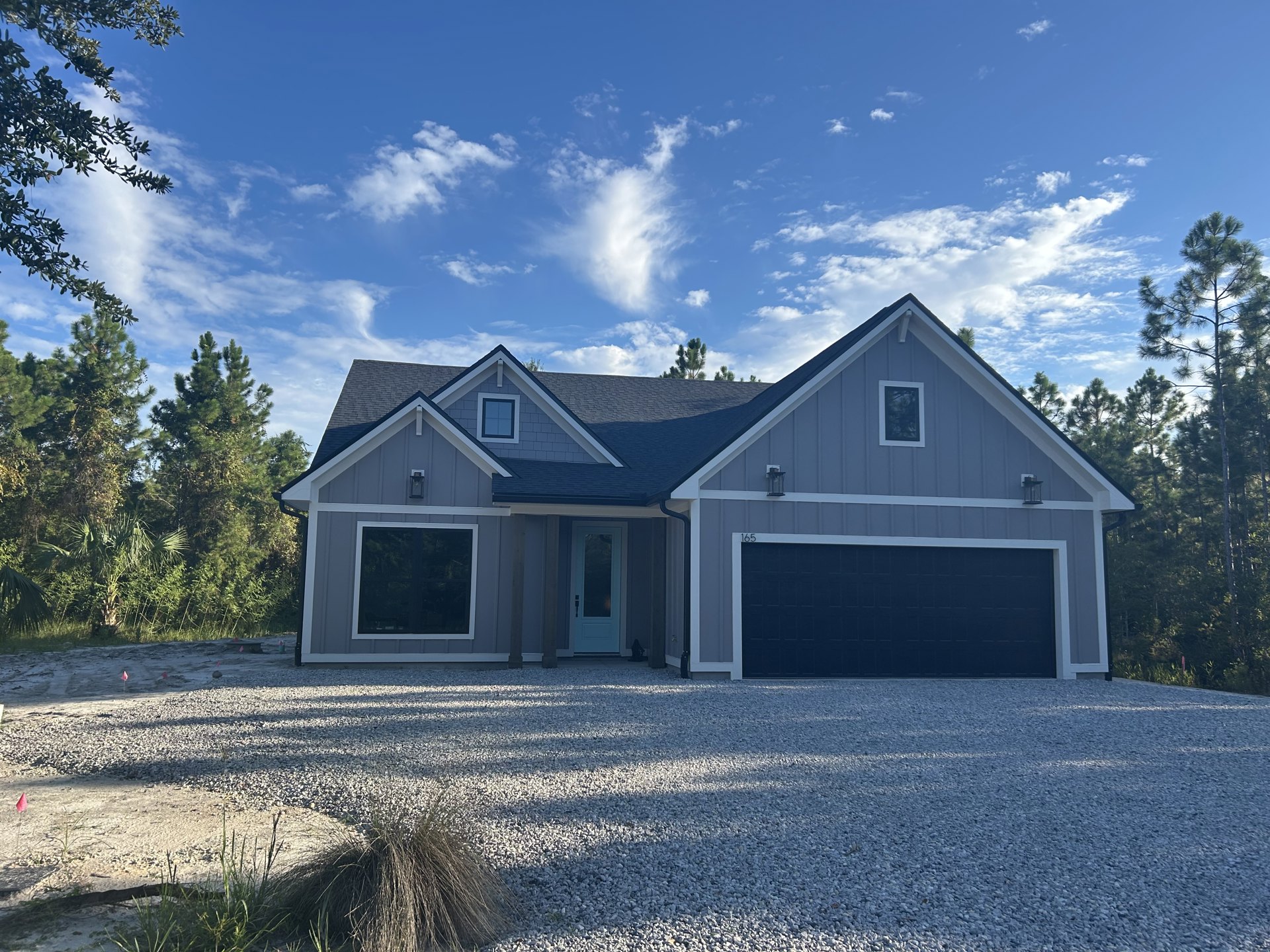 Two-story house with attached garage, blue siding, white trim, large windows, driveway, and partly cloudy sky overhead