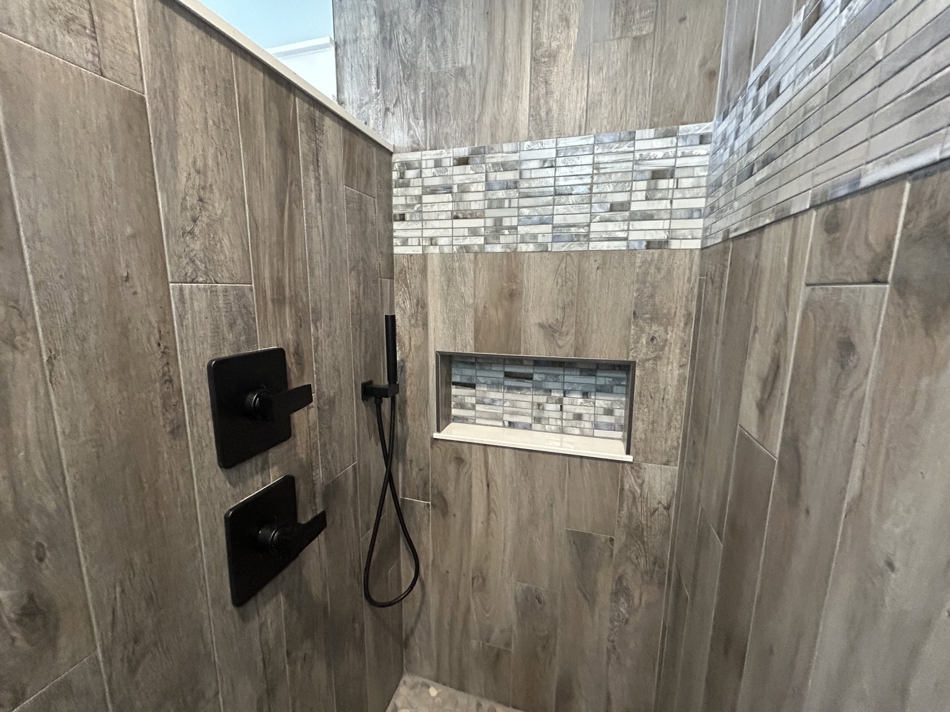 Modern shower with two matte black shower heads mounted on white tile wall, black metal fixtures, and wood accents