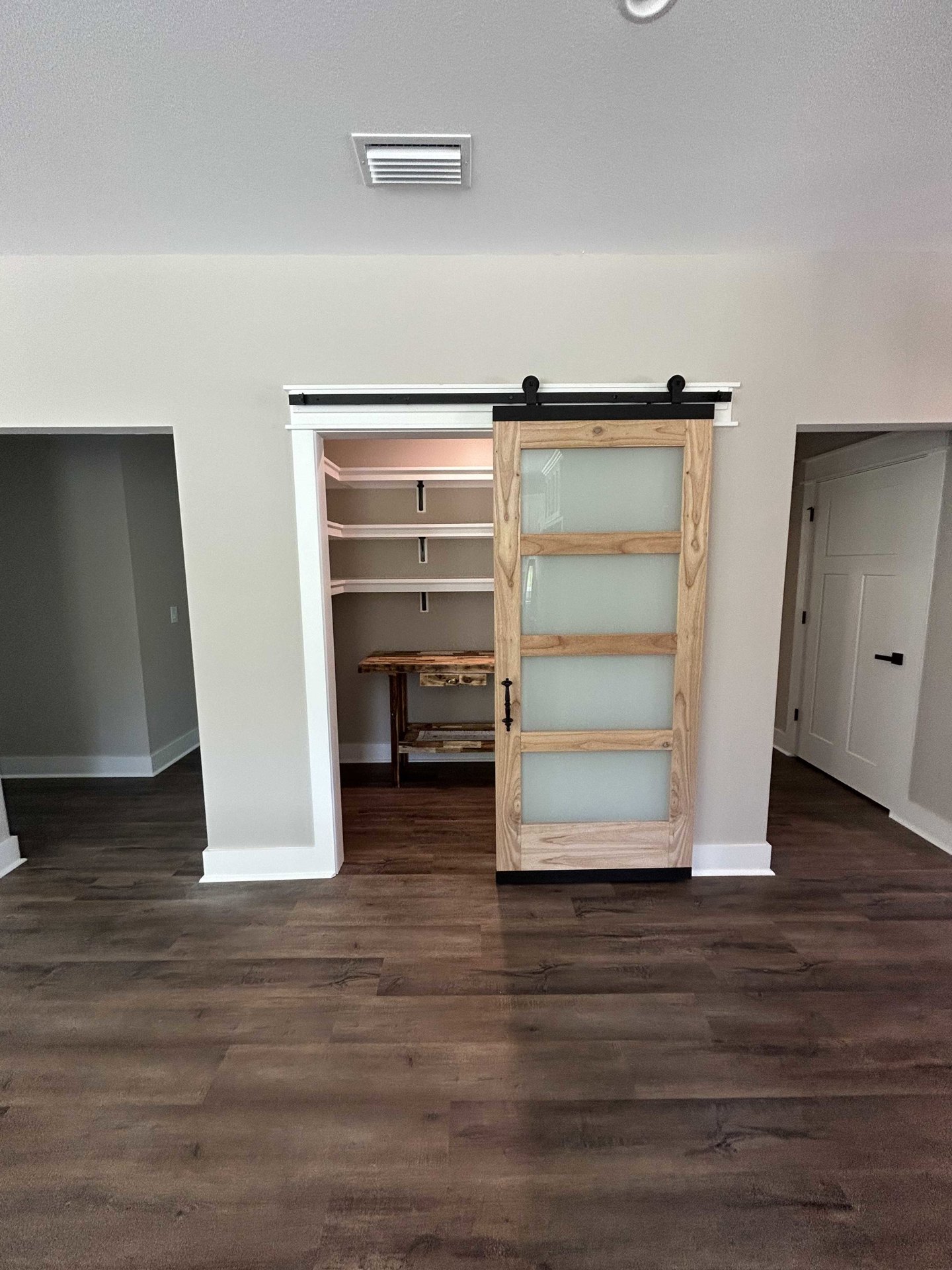 White sliding closet door with frosted glass panels and black handle, wood floor, wall vent, built-in shelving, and cabinetry.