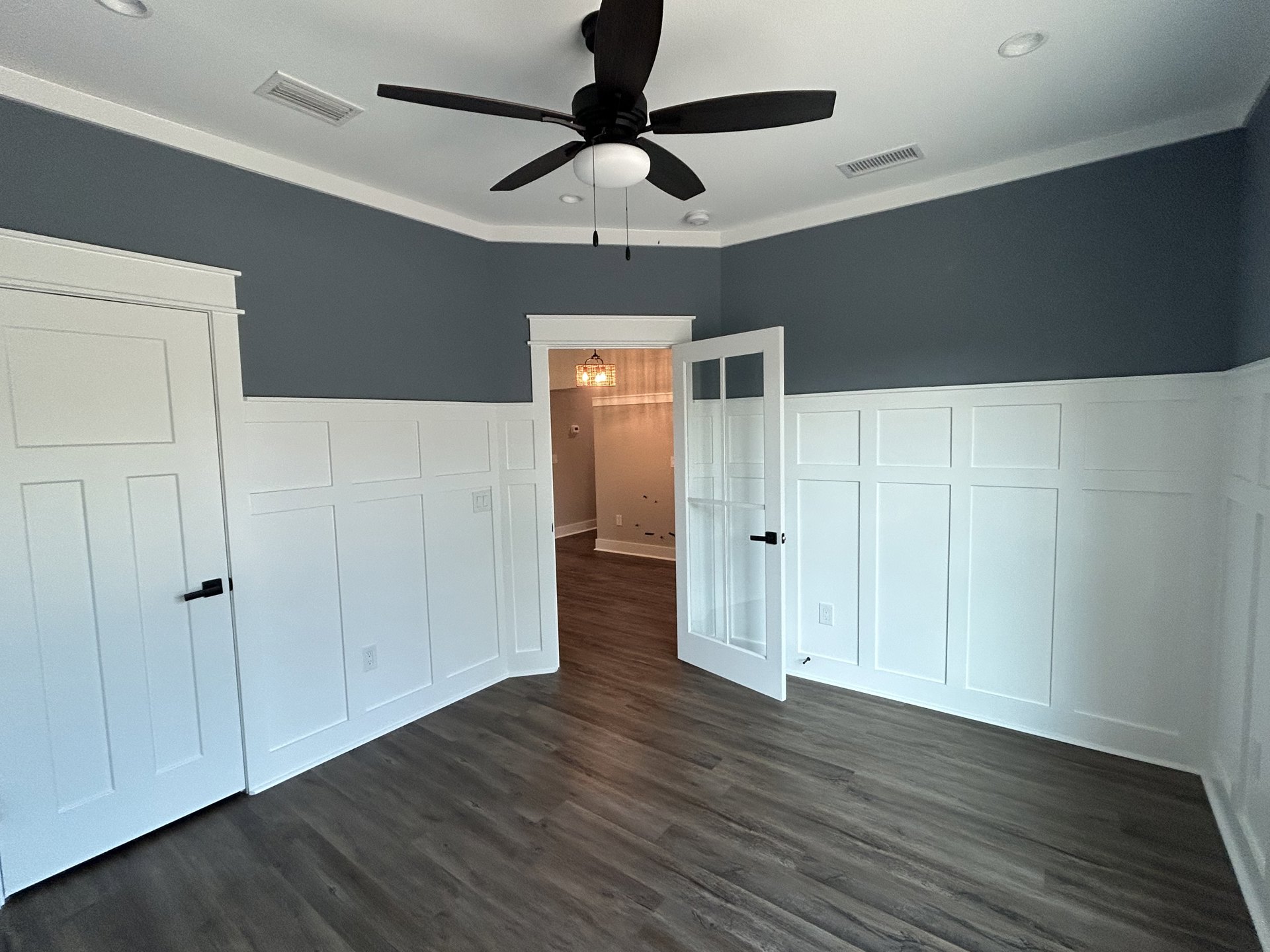White walls, wood flooring, ceiling fan with light fixture, white door featuring black handle