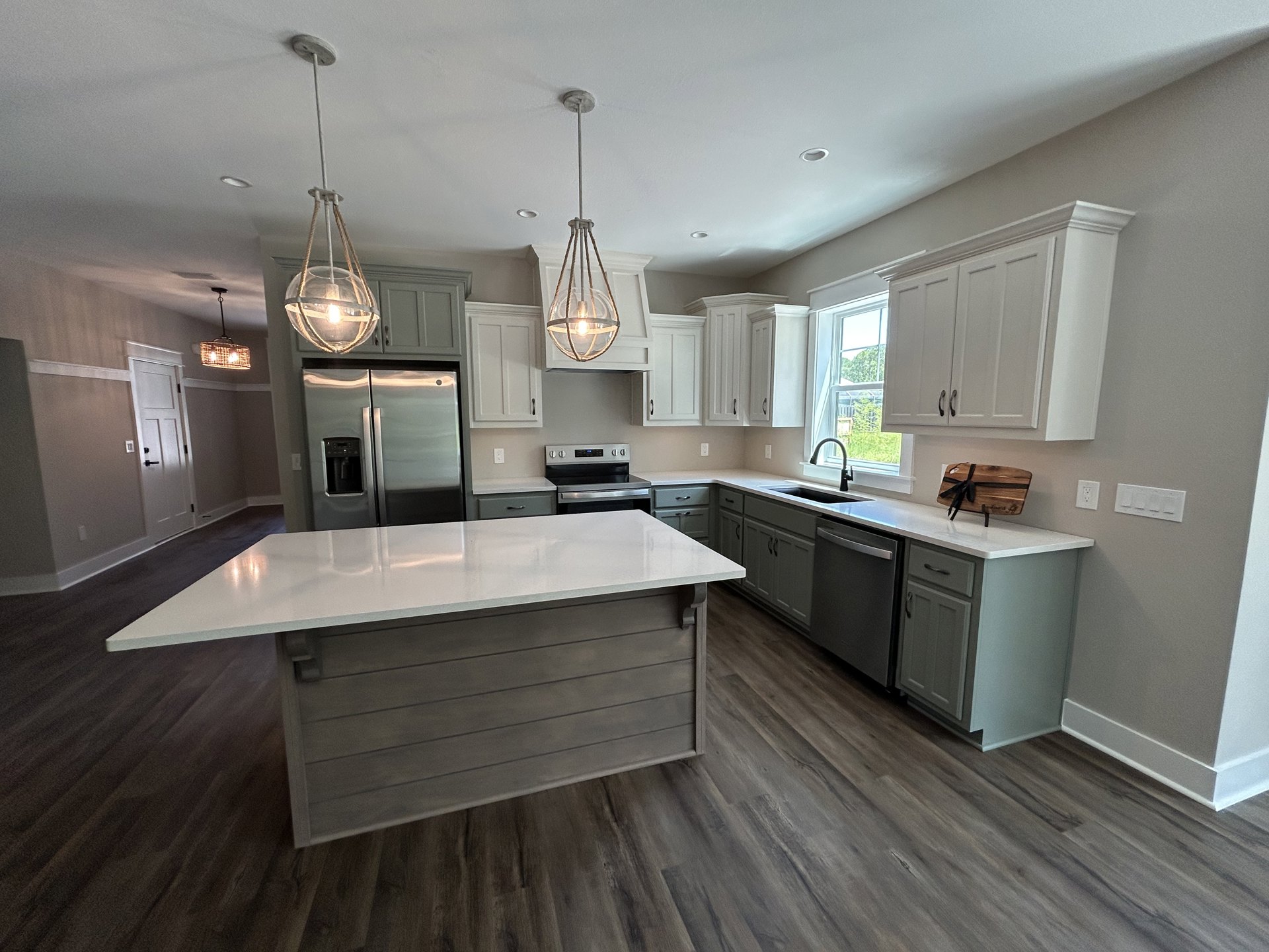 Spacious kitchen featuring a large white quartz island, stainless steel refrigerator with water dispenser, light wood cabinetry, built-in oven, and polished tile flooring