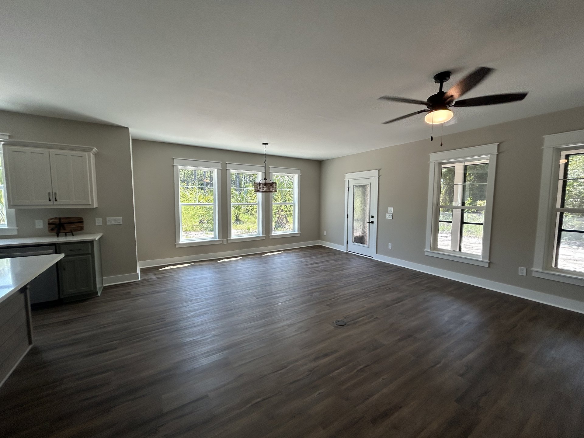 Spacious room with wood flooring, white-framed windows, glass-paneled door, and ceiling fan with light fixture