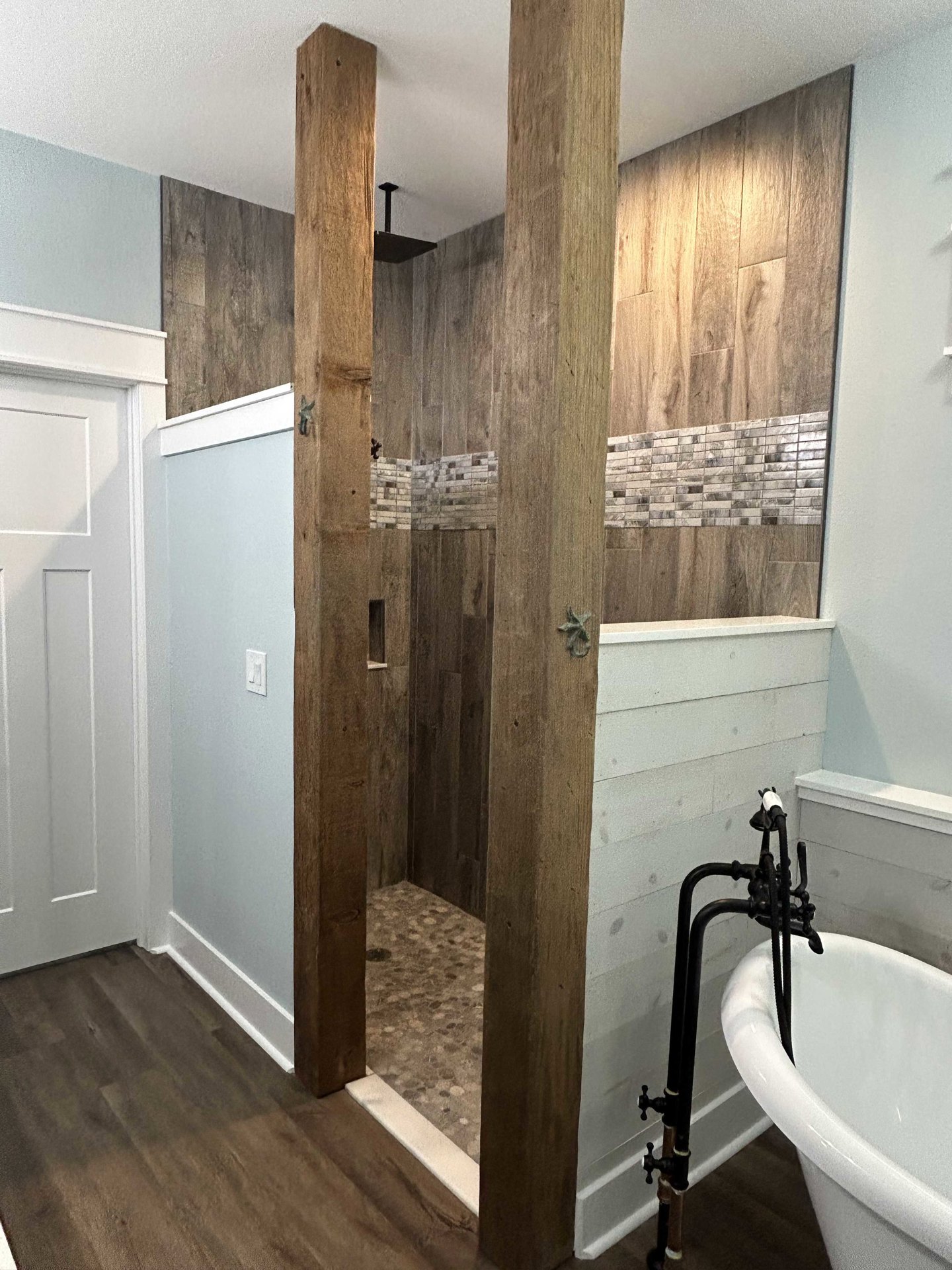 Bathroom featuring wood-paneled shower, freestanding white tub with black faucet, white walls, and modern light switch