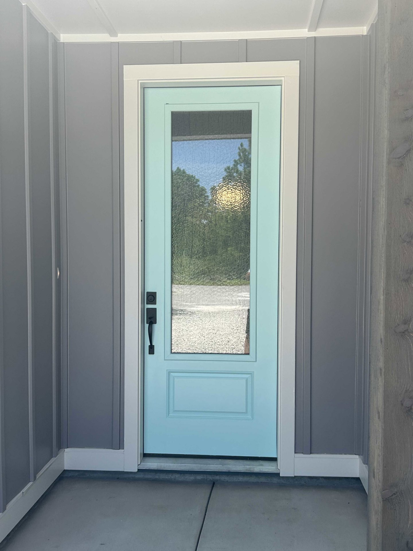 Blue door with vertical glass panel, silver door handle, white trim, and light-colored interior walls and floor