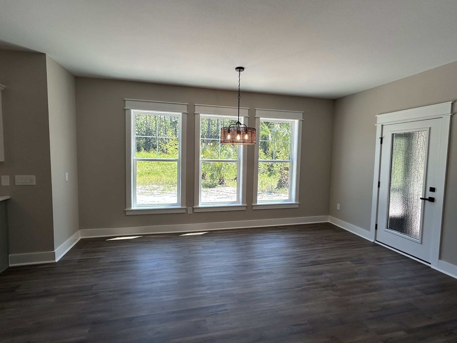 Chandelier hanging from ceiling above hardwood floor, large windows with tree views, glass-panel door, plaster walls