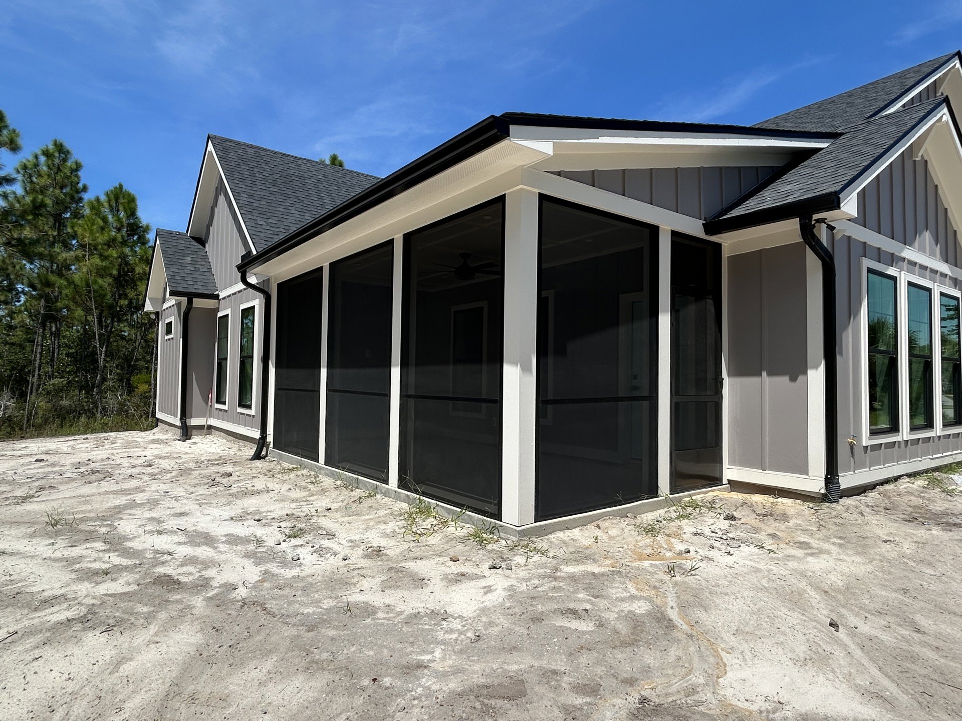 White custom home with black-framed windows, screen door entry, light siding, grassy yard, and mature trees reflected in glass.