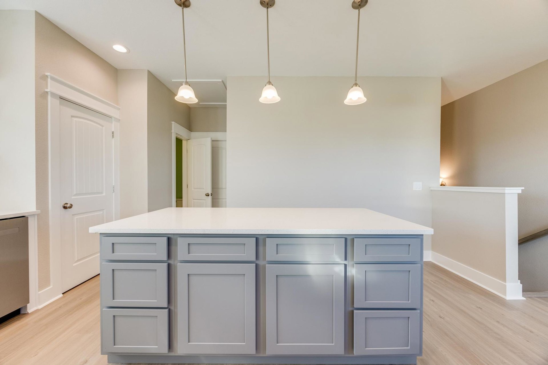 White kitchen island with white cabinets, black handles, and pendant lights hanging from ceiling; white walls with brown trim and light wood flooring.