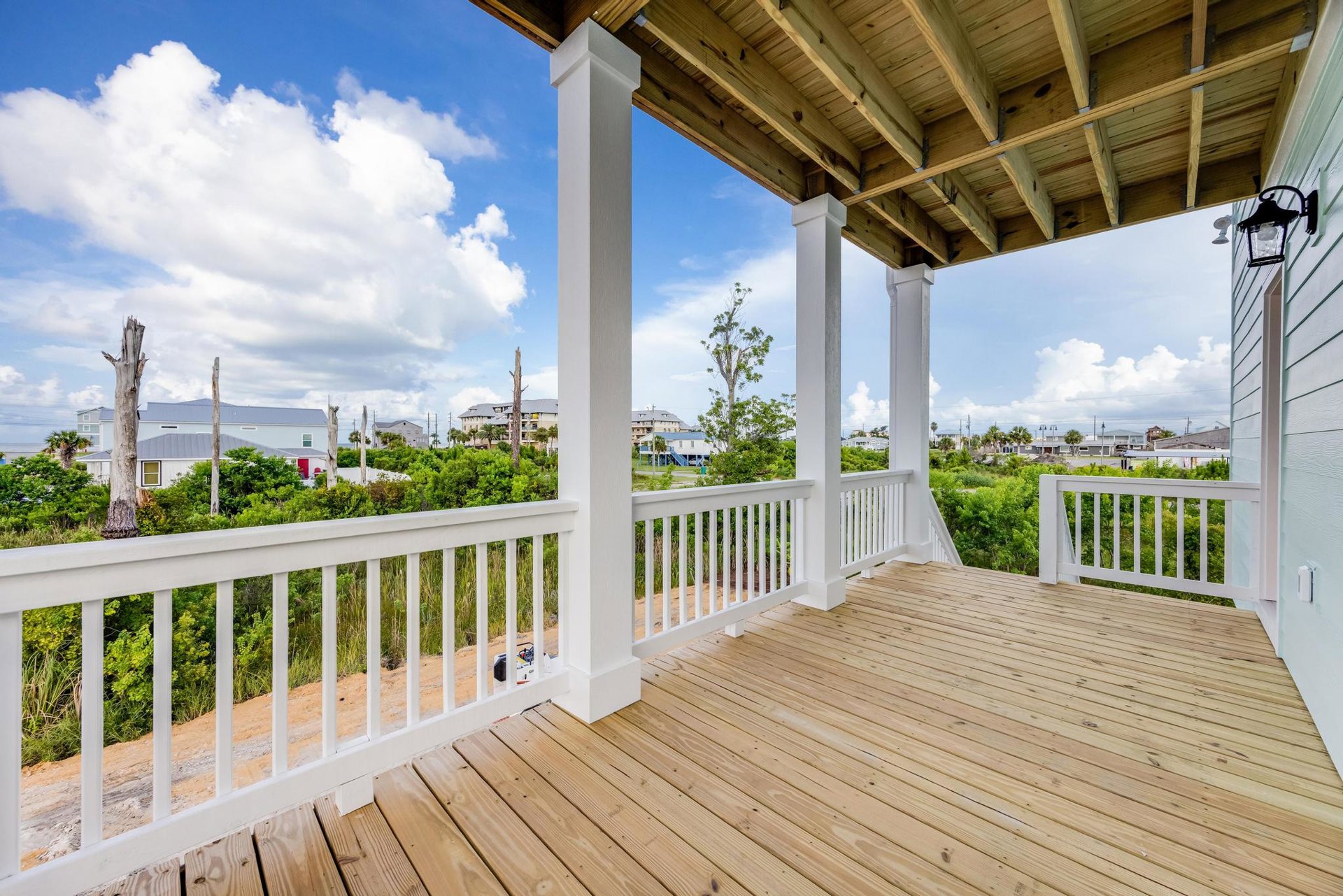 Wood deck with white pillar railings overlooking trees and blue sky