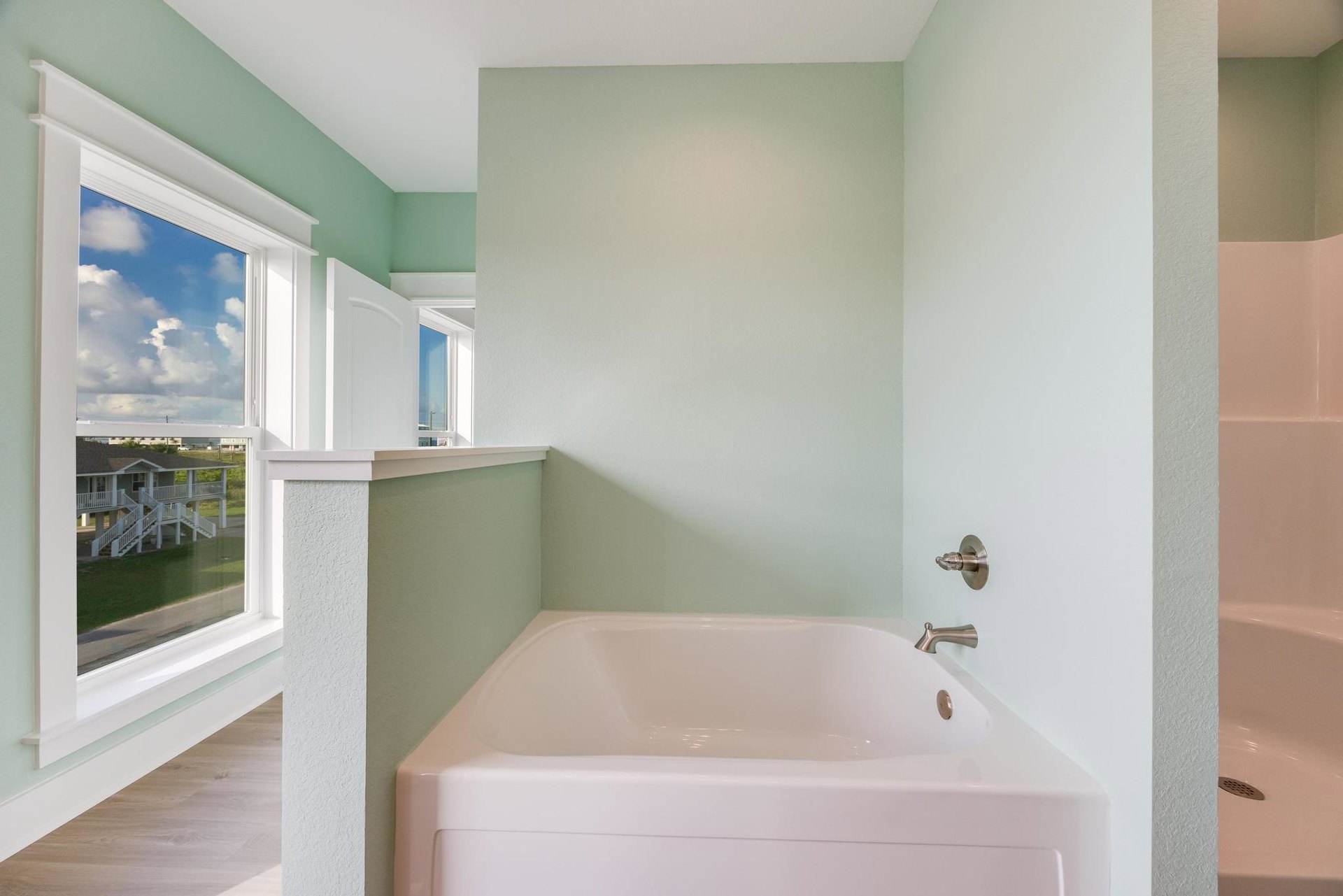 Freestanding white bathtub with chrome faucet against green accent wall, surrounded by light tile flooring and modern bathroom fixtures