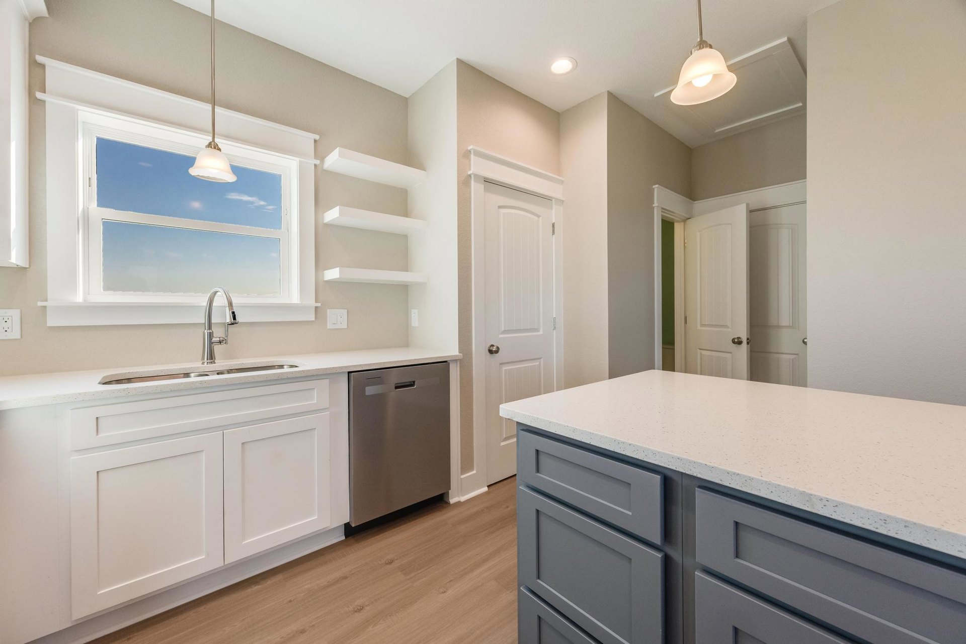 Modern kitchen featuring tile backsplash, white cabinetry, stainless steel sink with chrome faucet, built-in dishwasher, stone countertop, and overhead pendant lighting