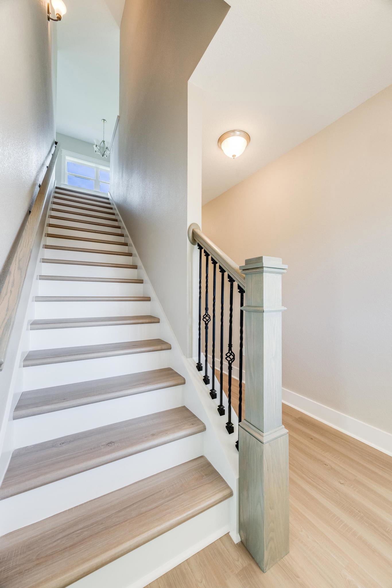 Wood staircase with black metal railing, white pillar, light fixture on ceiling, and hardwood flooring in a residential interior.