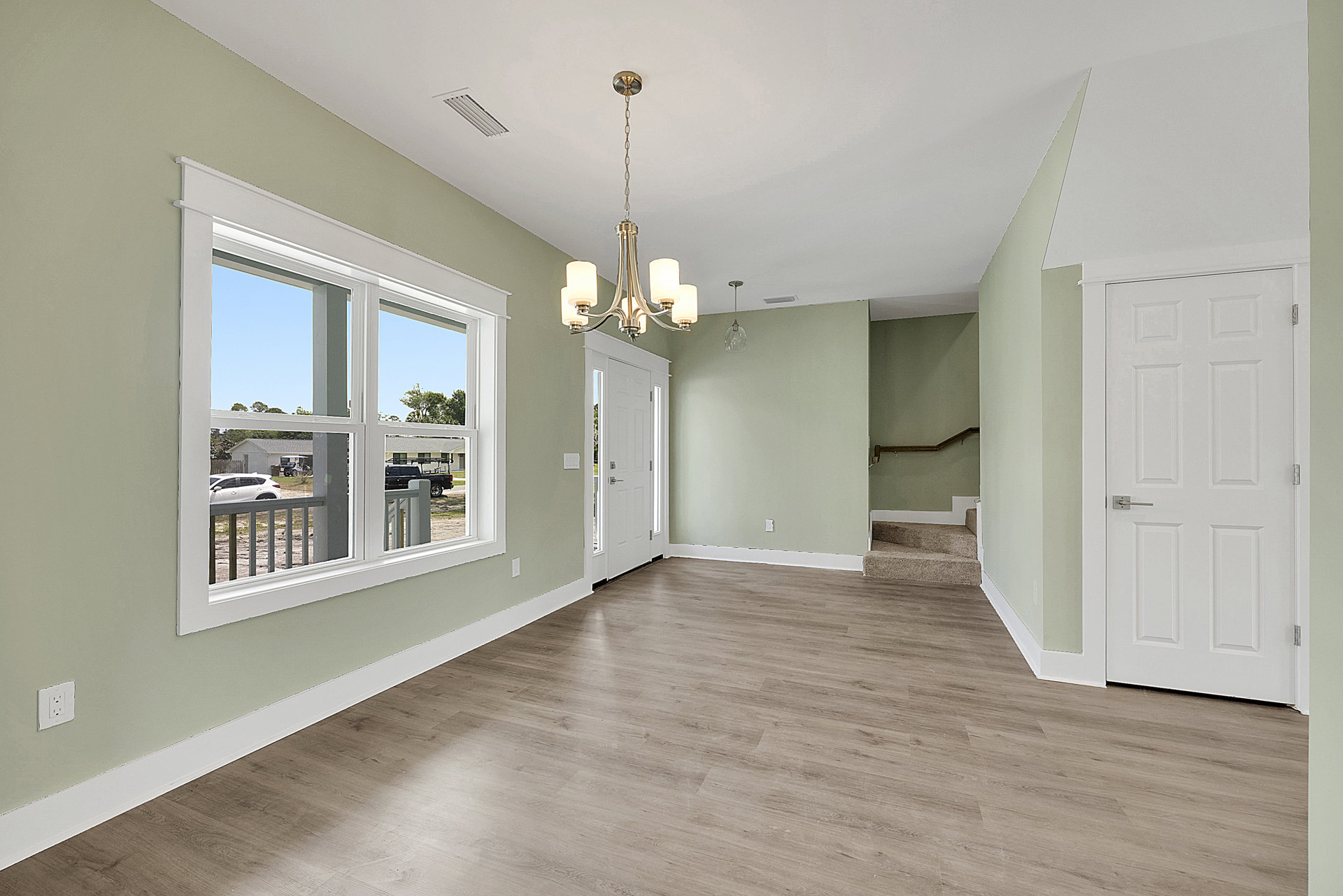 Room with wood flooring, white walls, white door with silver handle, and a chandelier-style light fixture