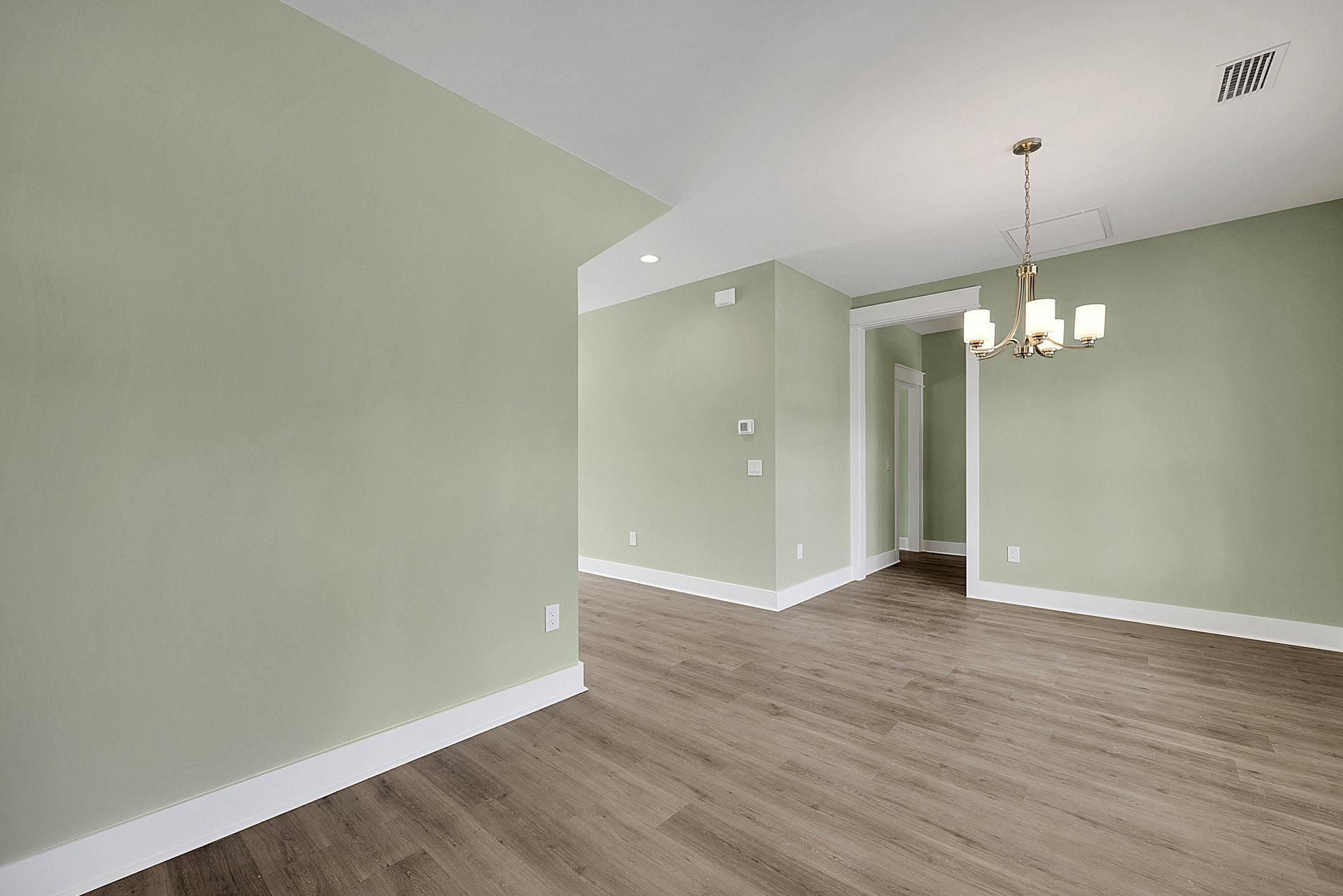 Green-painted walls, wood flooring with white trim, ceiling chandelier, wall vent, rectangular floor pattern